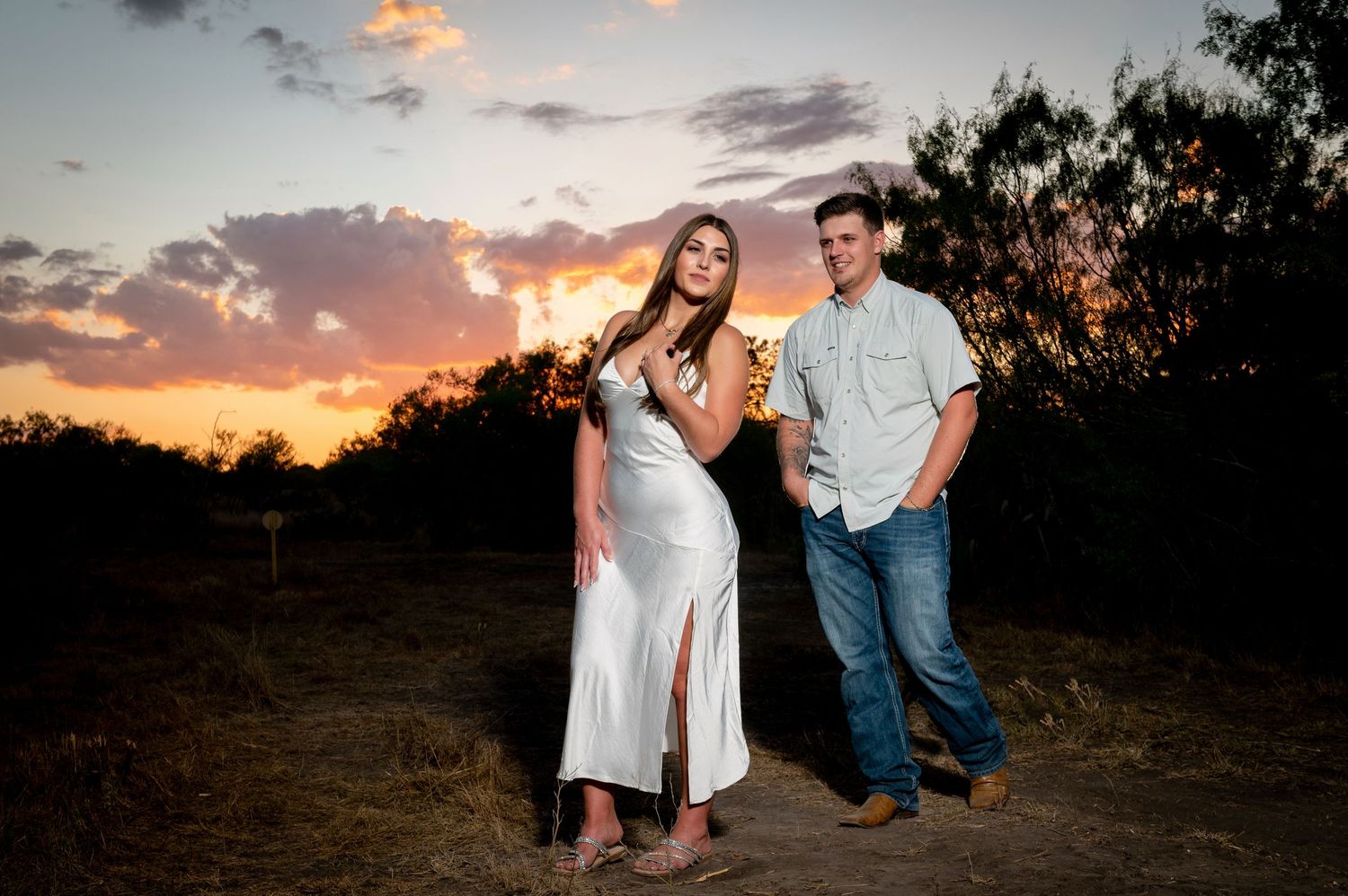 Stylish couple posing in casual elegance against vibrant sunset backdrop.