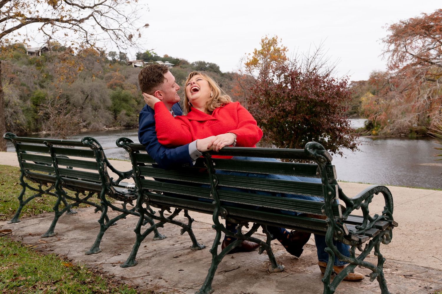 A couple shares a tender moment on a park bench by a lake in autumn.