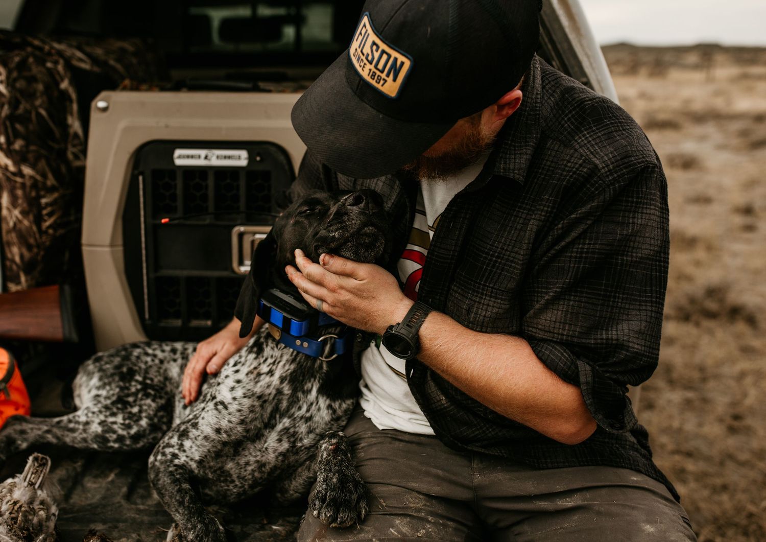 image of upland bird hunter sitting on tailgate petting his bird dog