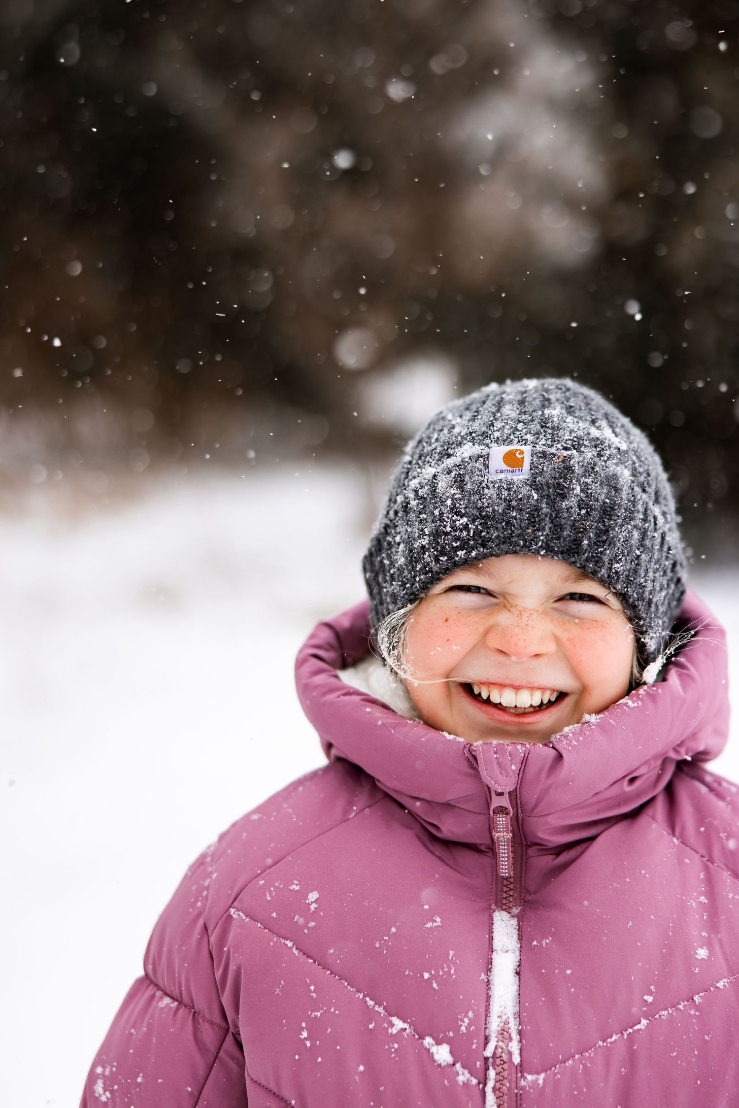 Girl in the snow wearing a carhartt stocking hat and pink jacket