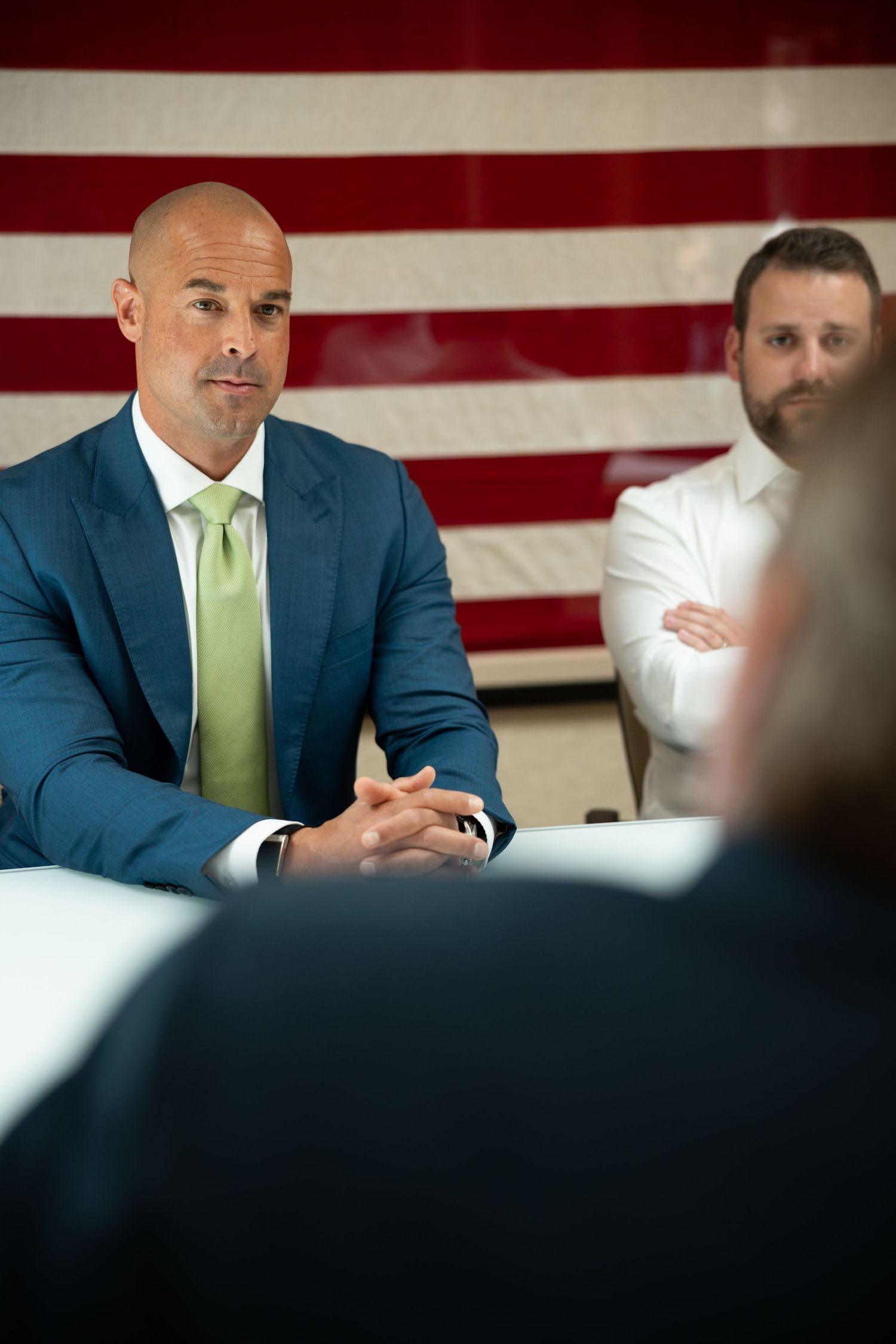 image of man in suit at conference table in front of flag