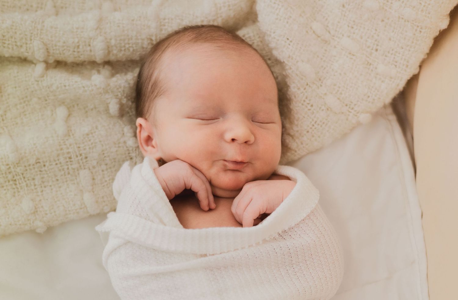 Peaceful newborn baby sleeping swaddled in white blanket.