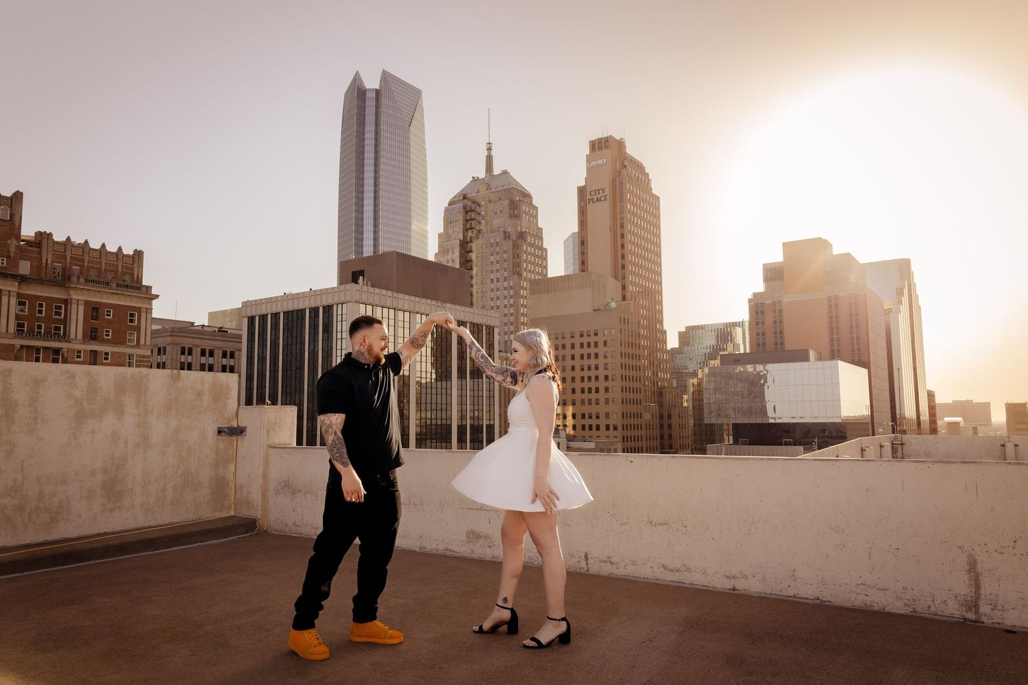 Couple dancing on rooftop with Oklahoma City skyline at golden hour.