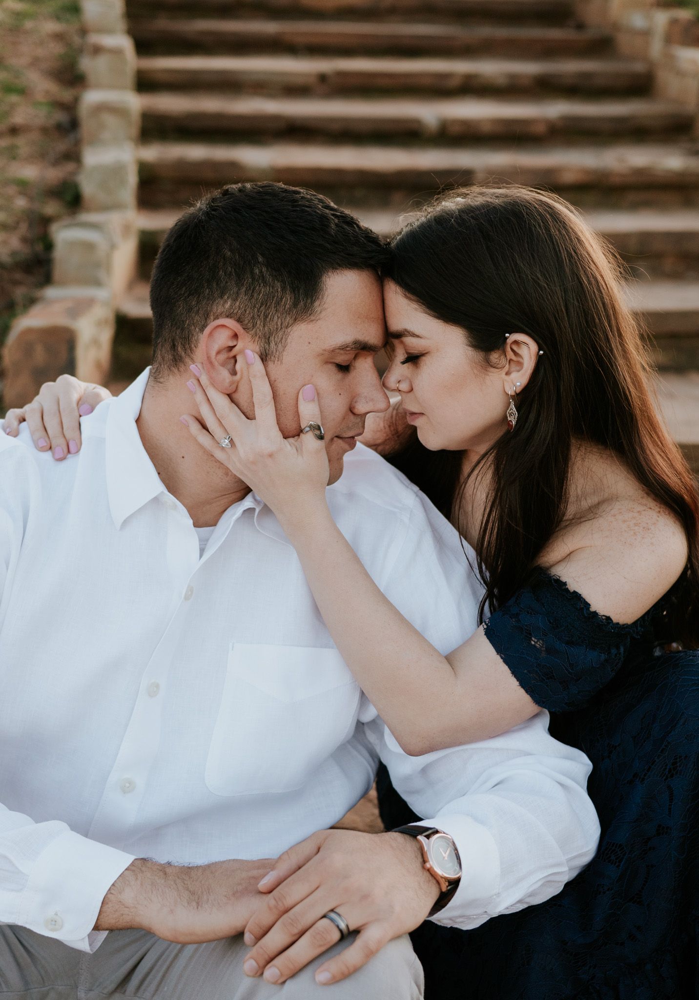 Engaged couple sharing intimate moment with foreheads together, woman wearing diamond ring and off-shoulder dress.