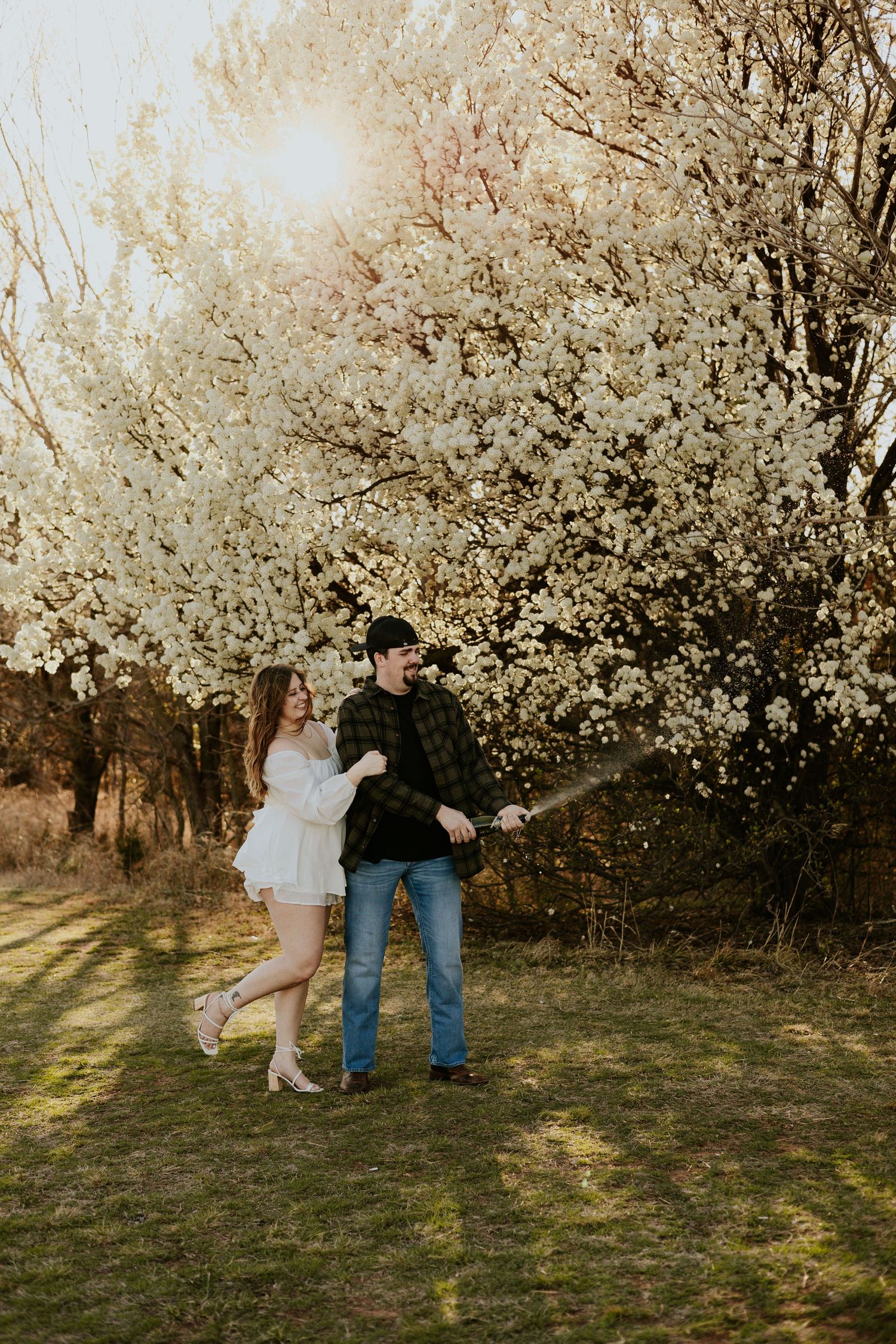 Happy couple walking and laughing together beneath stunning white flowering trees at sunset.