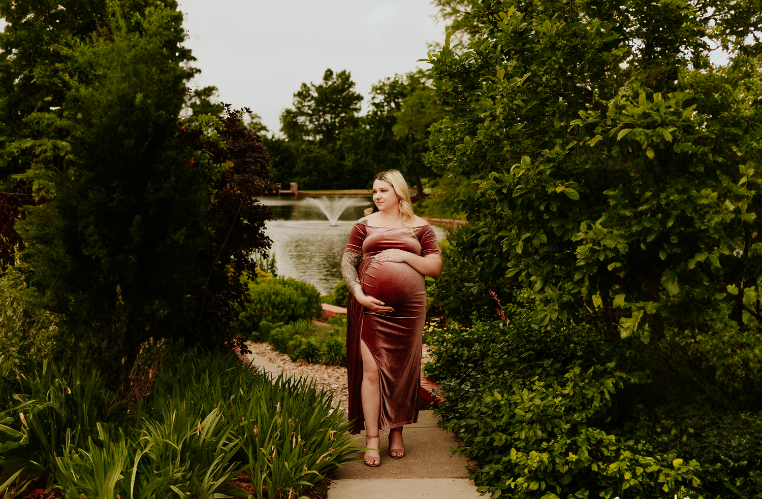 Expecting mother in a mauve maternity dress cradling her bump in a lush garden setting.
