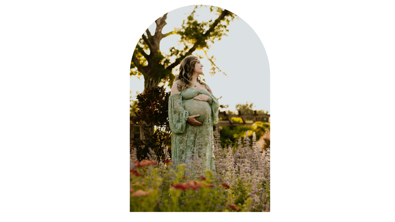 Pregnant woman in green floral dress standing in a blooming garden during golden hour.