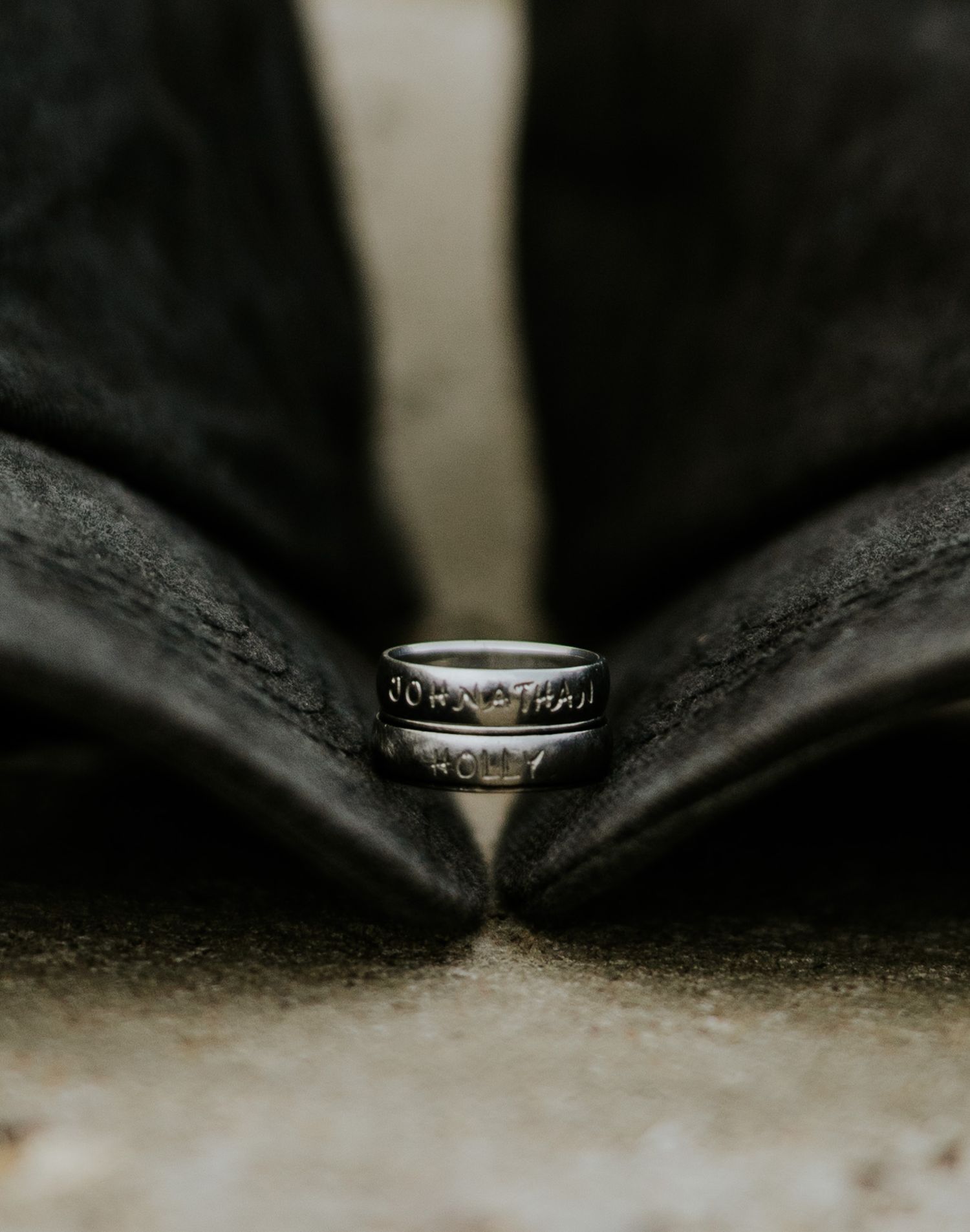 Close-up macro shot of engraved silver wedding bands nestled between two black leather shoes.