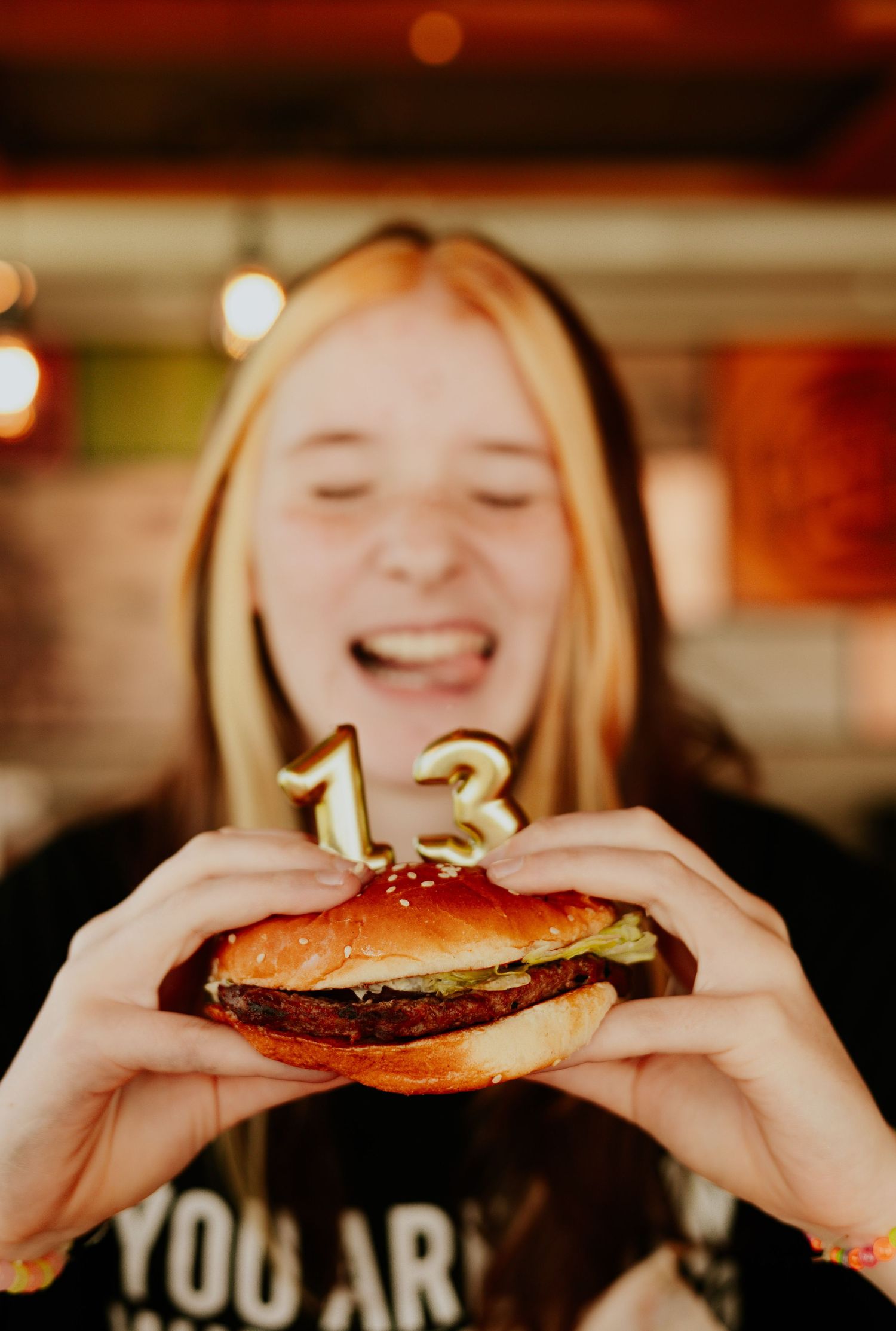 Teen girl laughing while holding a birthday burger with number 13 candles.