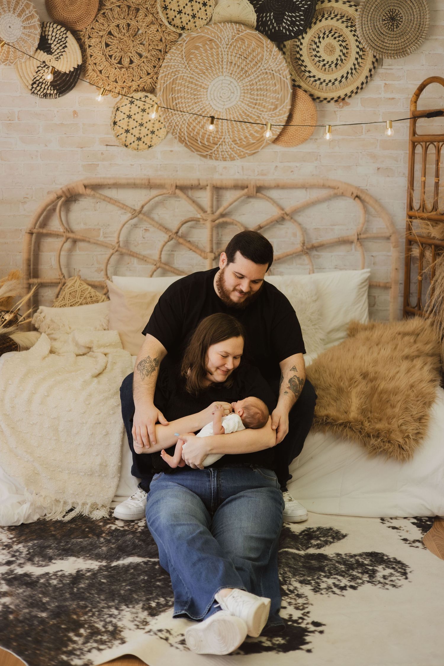 Parents sitting on bed holding newborn in boho-styled nursery.