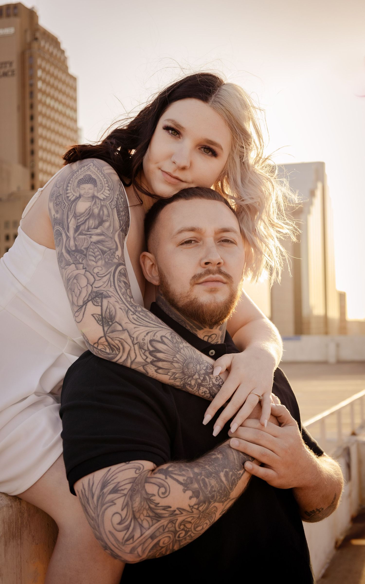 Couple embracing on rooftop with city skyline at golden hour.