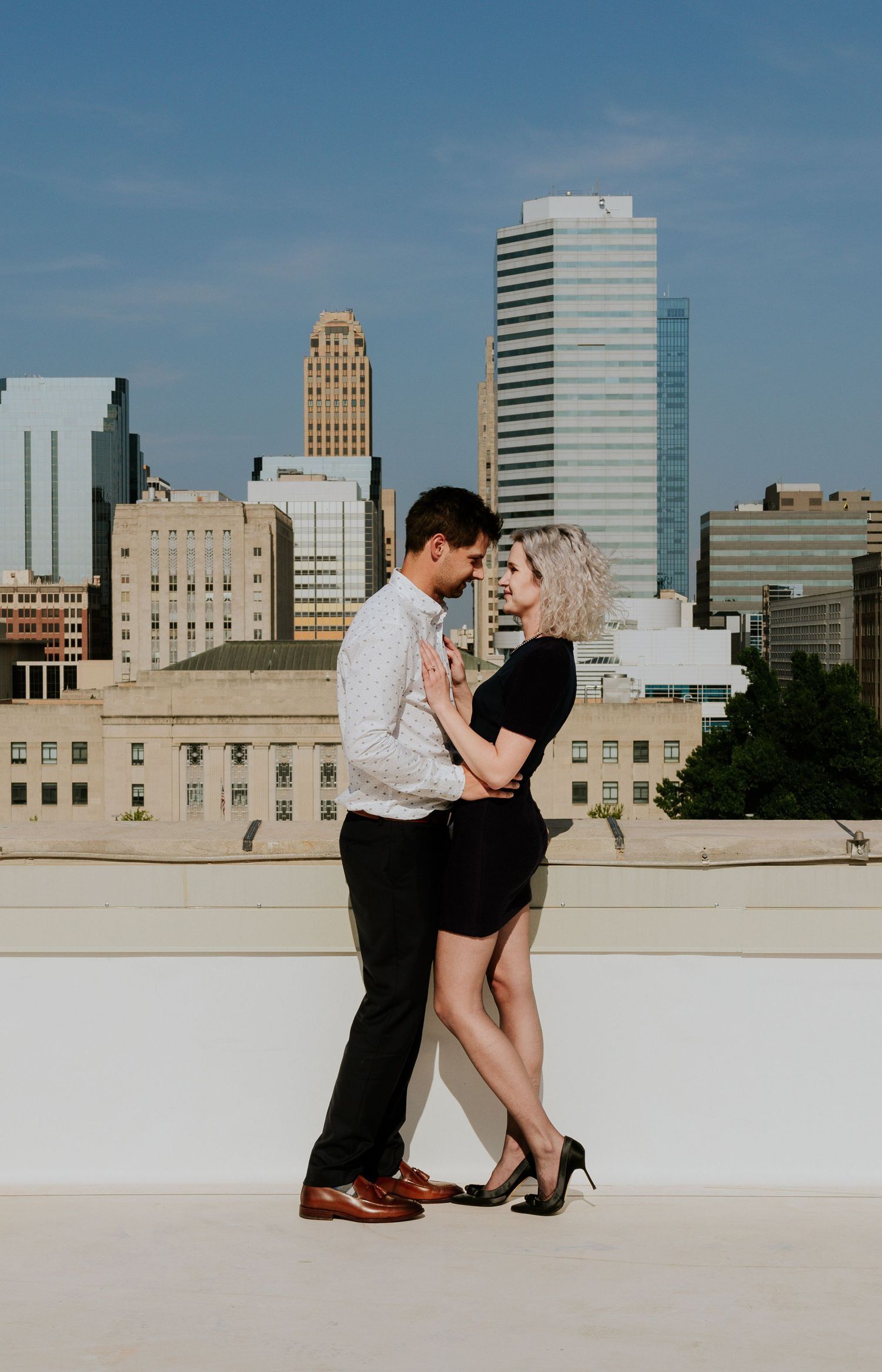 Couple in elegant attire sharing an intimate moment on a rooftop with city skyline backdrop.