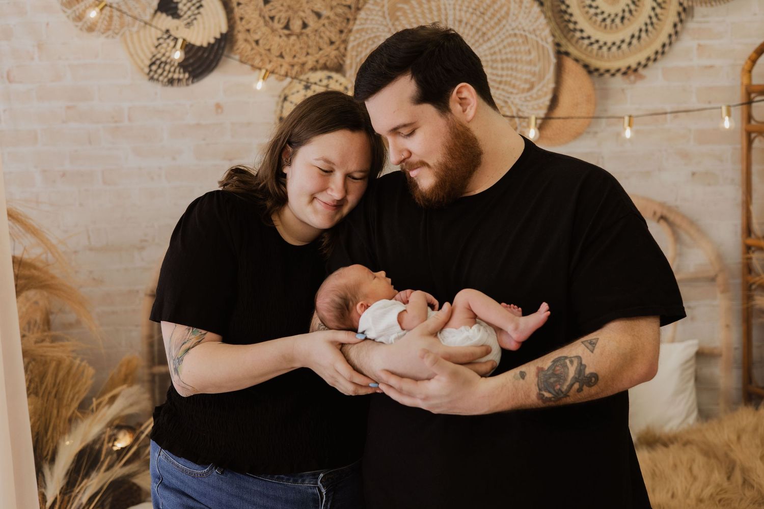 Parents holding newborn baby together in boho-decorated studio.