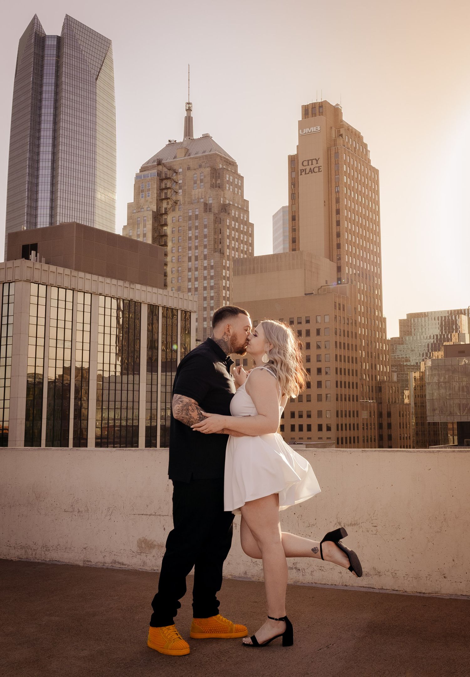 Couple kissing on rooftop with Oklahoma City skyline at golden hour.