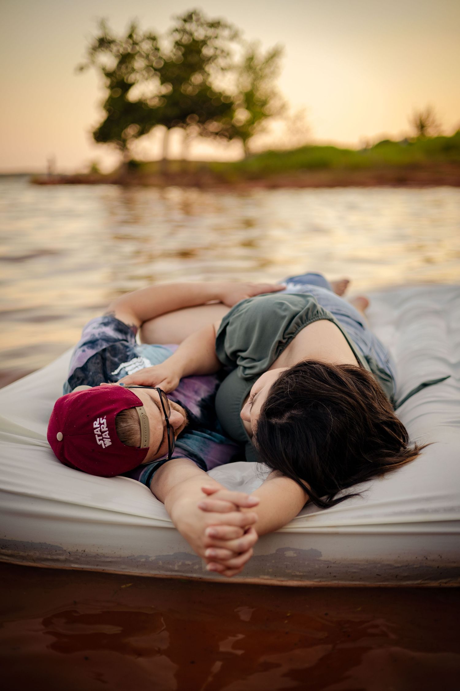 Couple cuddling closely on a floating raft on a peaceful lake during a golden sunset.