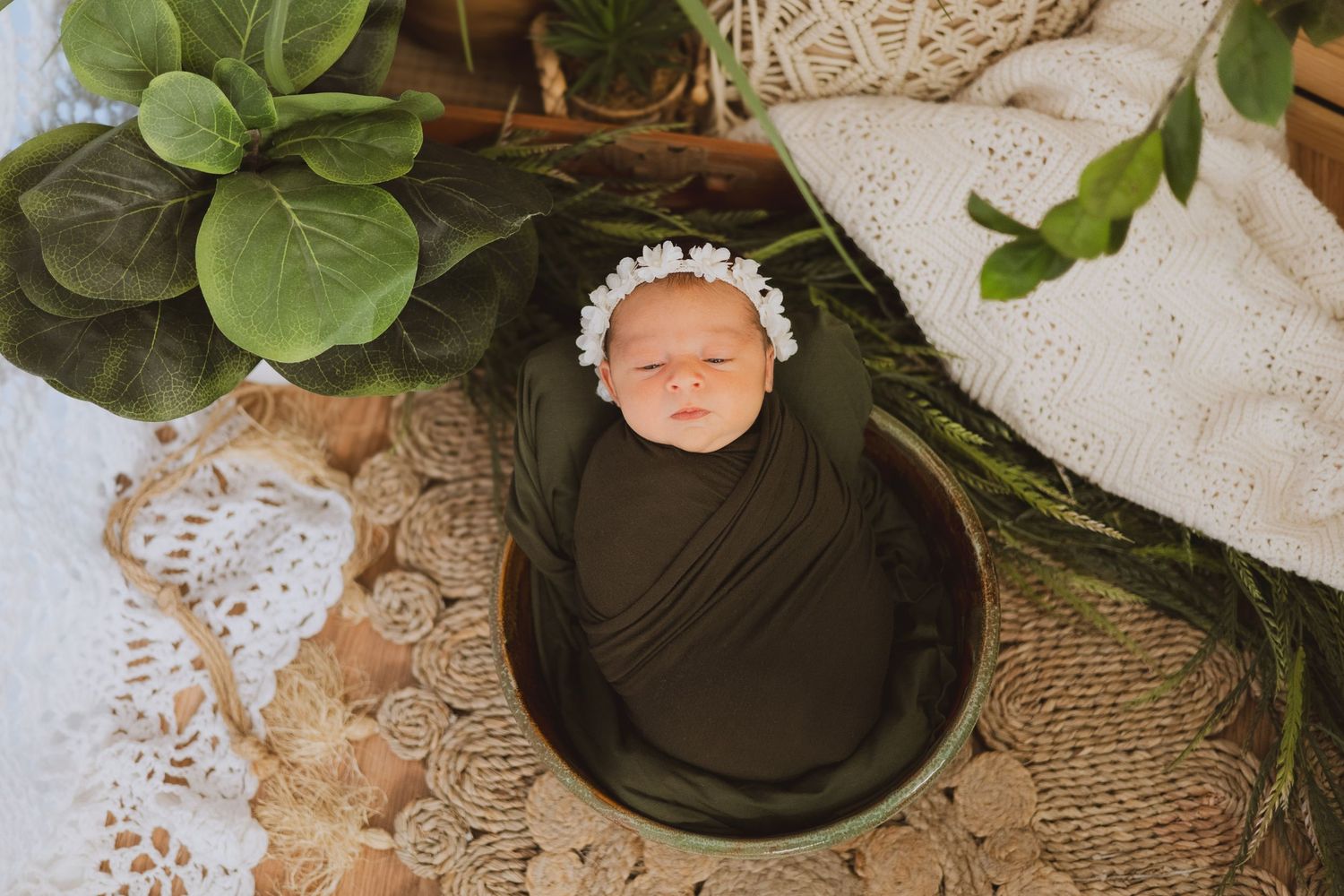Sleeping newborn baby swaddled in olive green wrap sitting in bucket with lace and greenery.