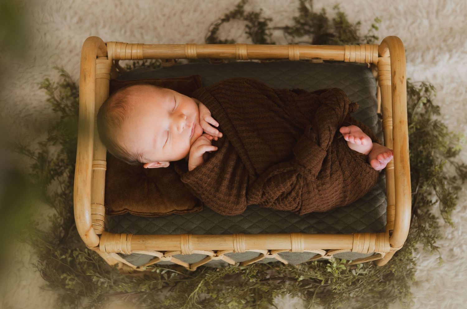 Overhead view of newborn baby in brown wrap lying in a wooden rattan crib.