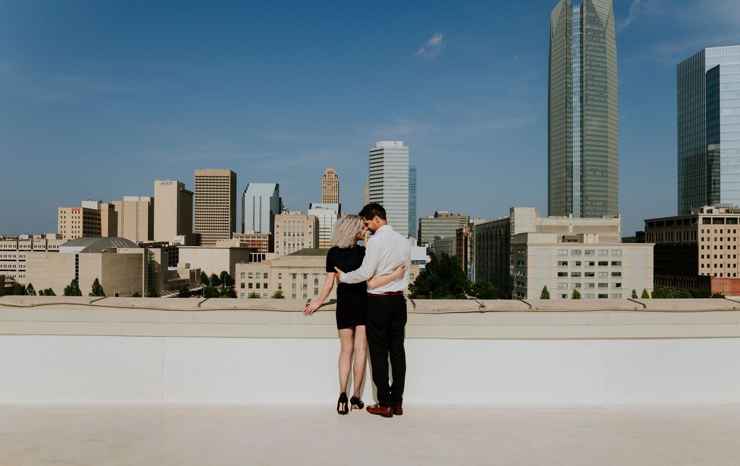 Couple sharing a tender embrace on a rooftop with an expansive city skyline on a sunny day.