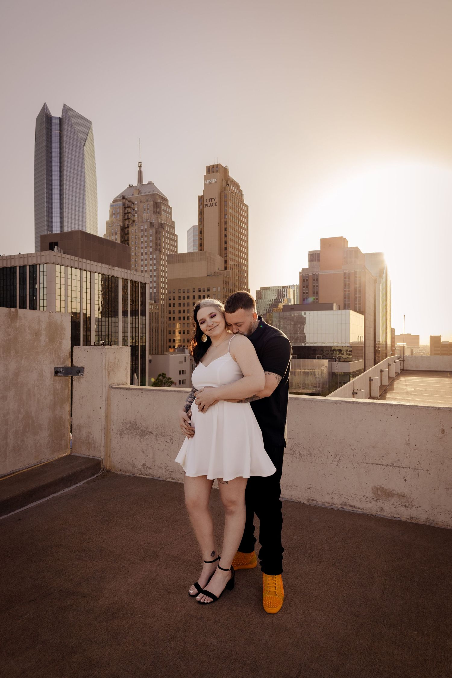 Couple embracing on rooftop at sunset with city skyline backdrop.