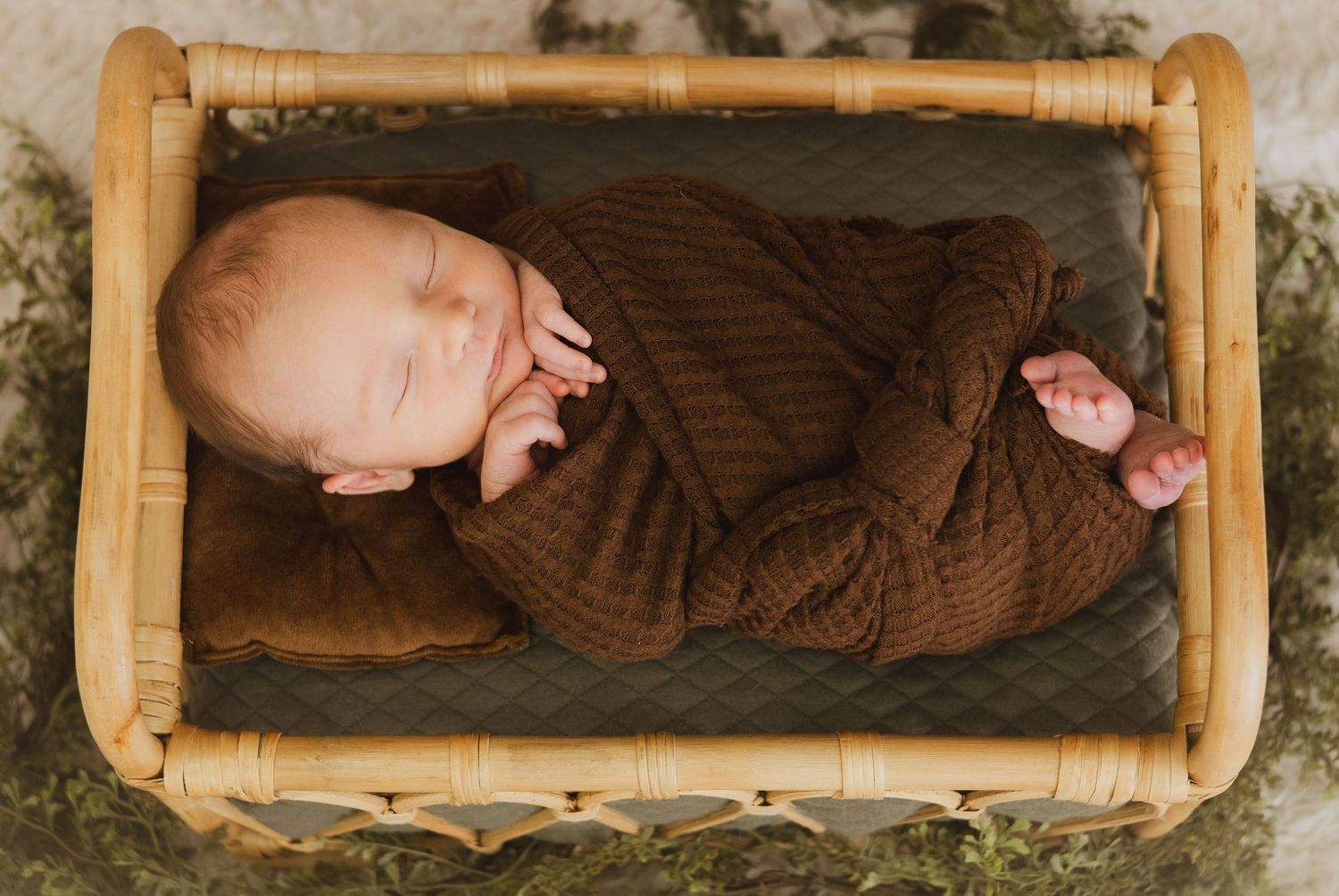 Newborn baby in brown knit wrap sleeping in a small wooden rattan crib.