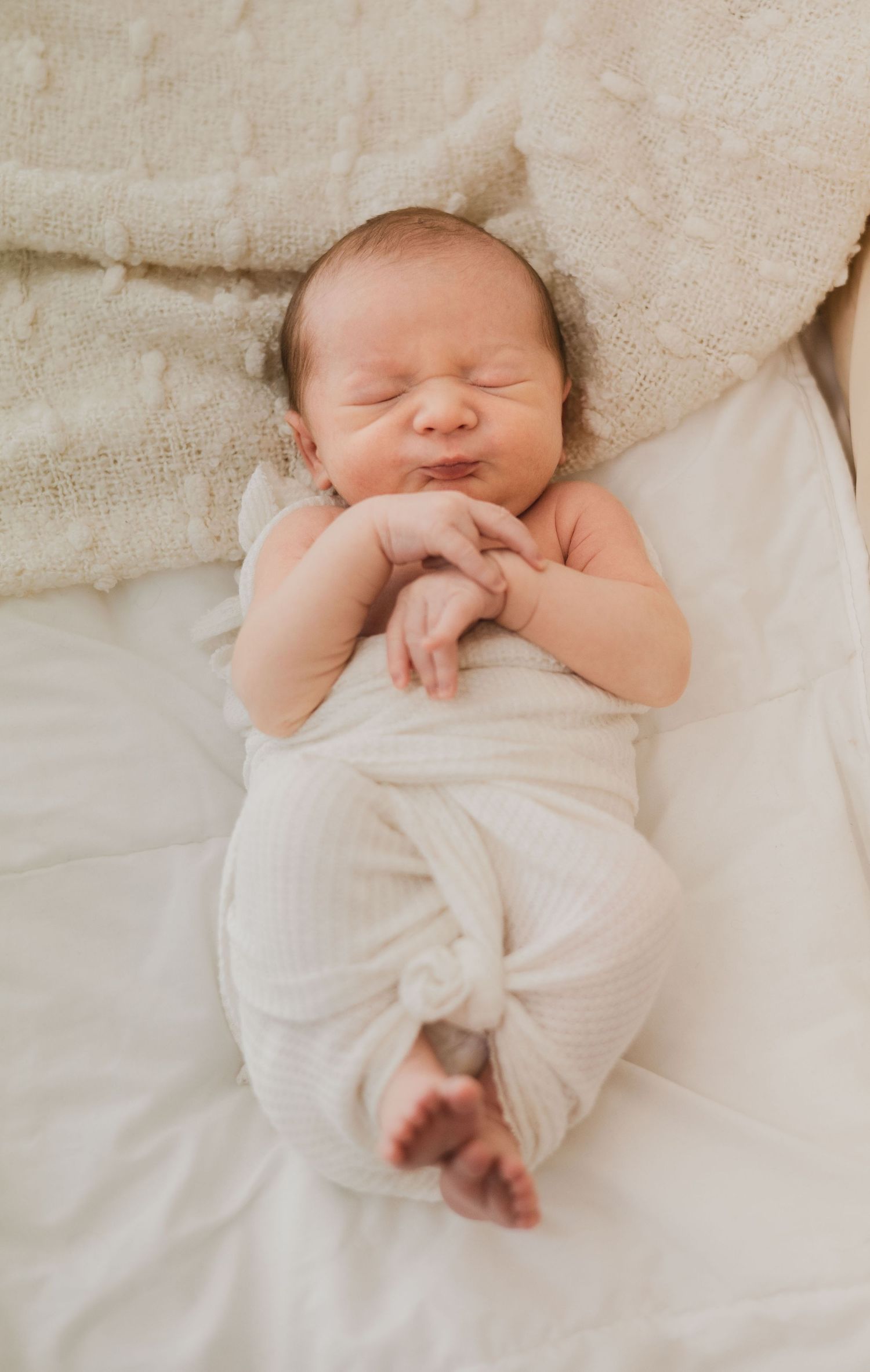 Smiling newborn baby lying in white swaddle on soft blanket.