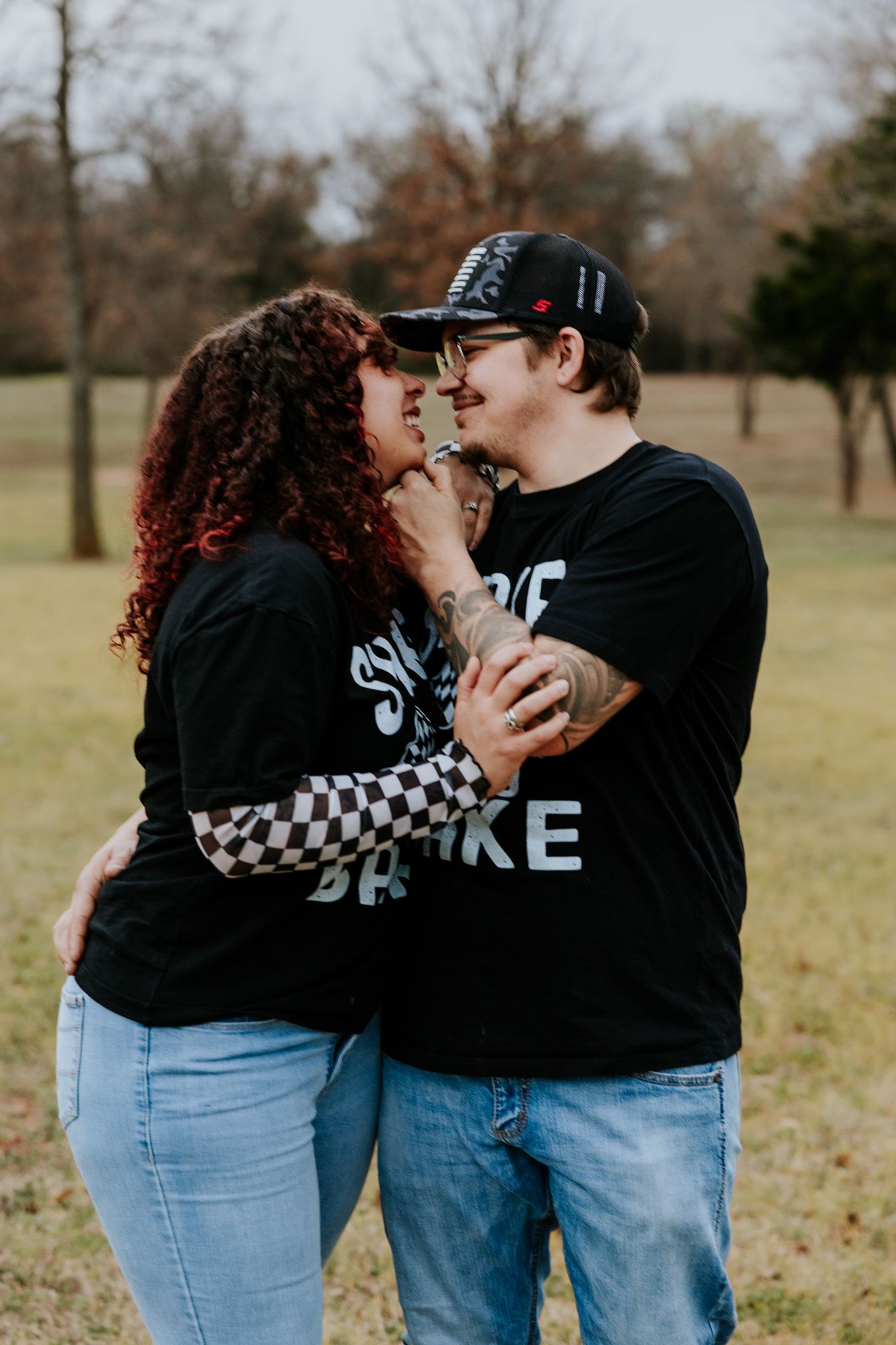 Couple in matching black graphic tees and jeans sharing a romantic moment in a winter park.