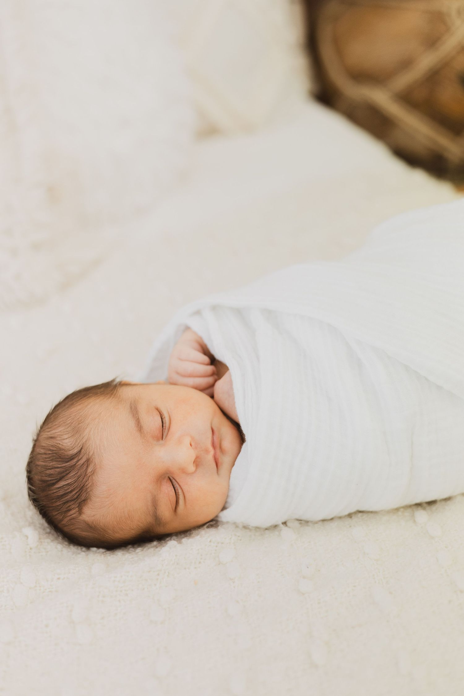 Peaceful newborn baby swaddled in white wrap sleeping on soft white blanket.