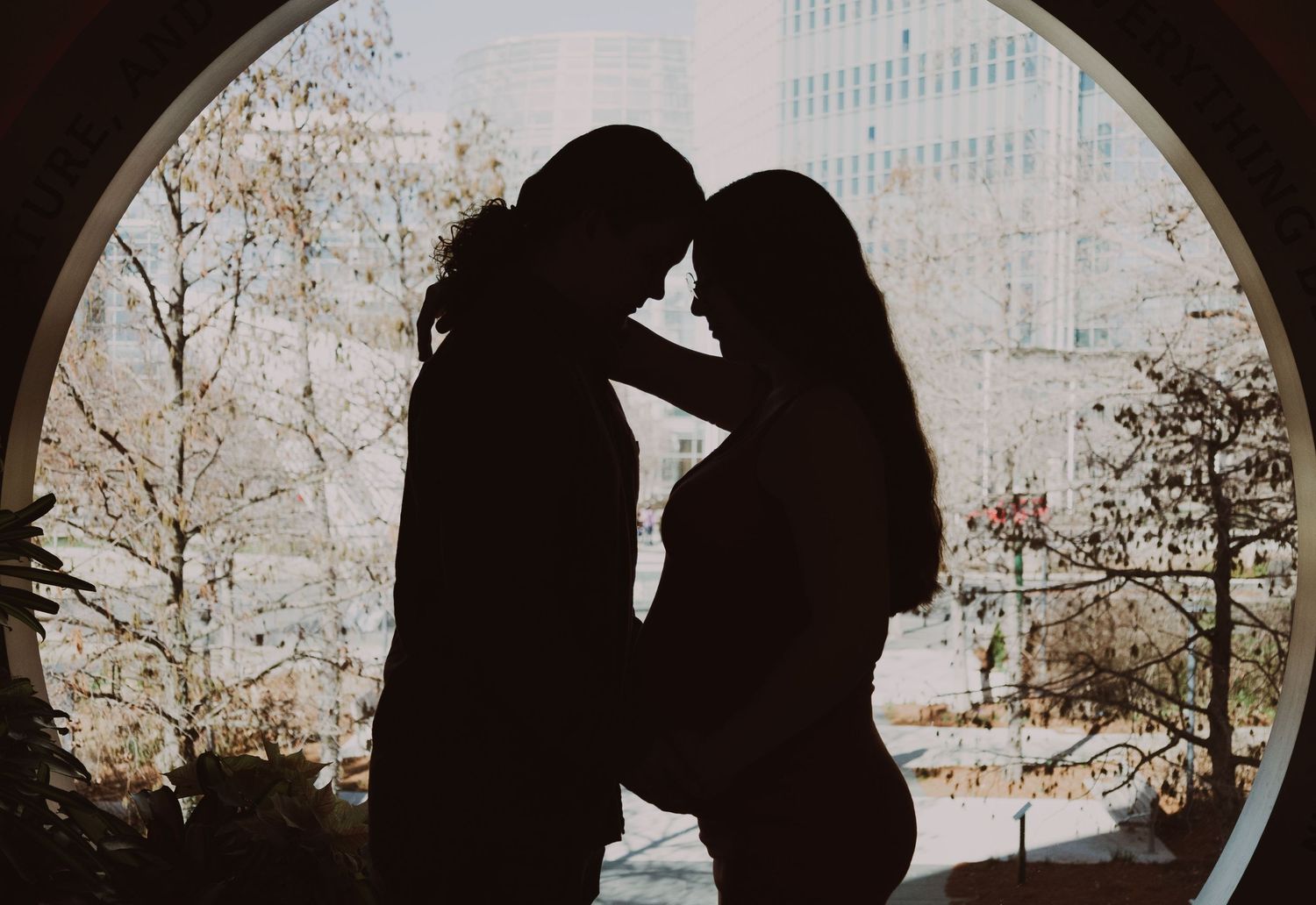Romantic silhouette of a couple touching foreheads framed by a circular window with city views.