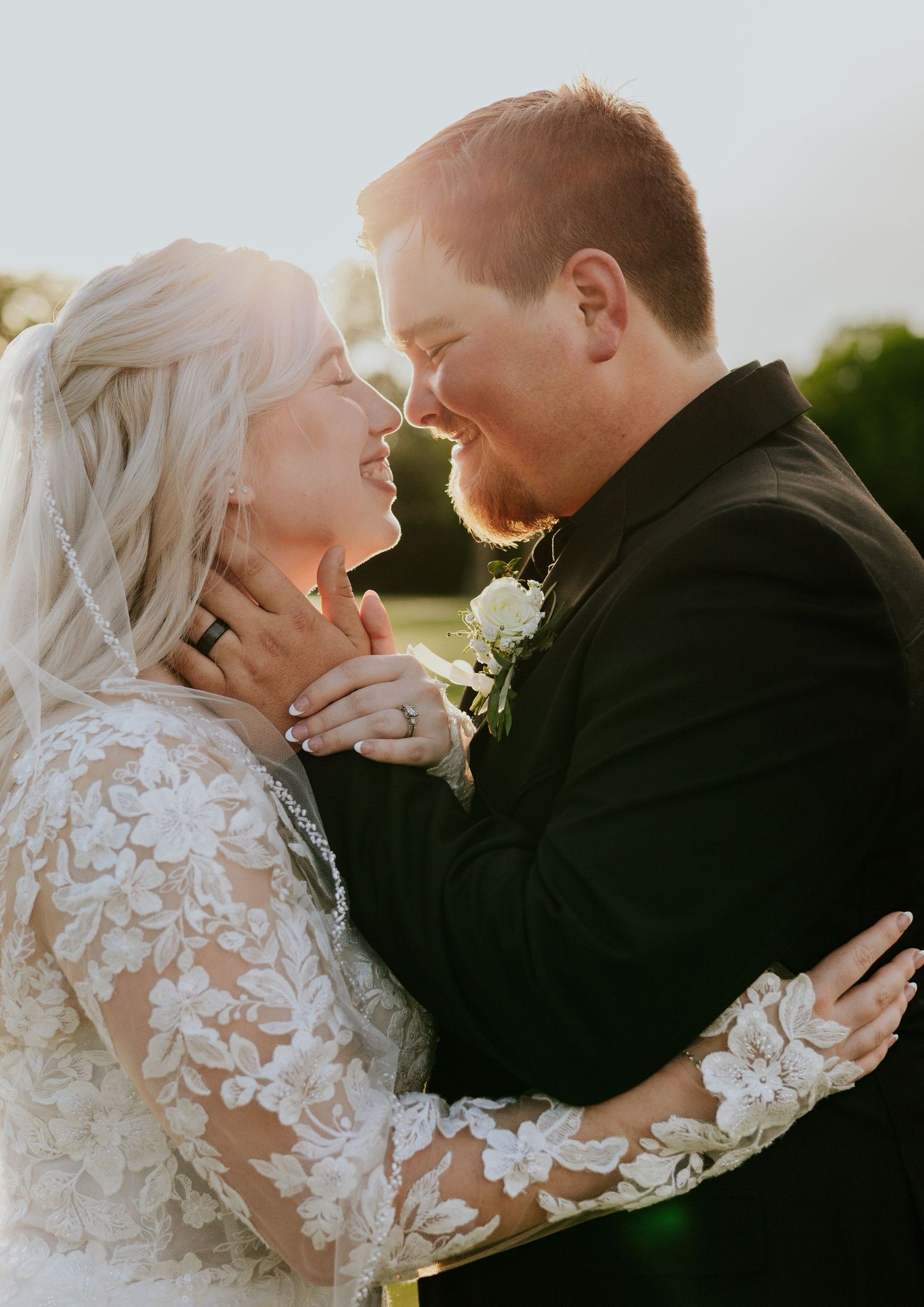 Bride and groom sharing a joyful intimate moment in golden hour sunlight, bride in lace wedding gown.
