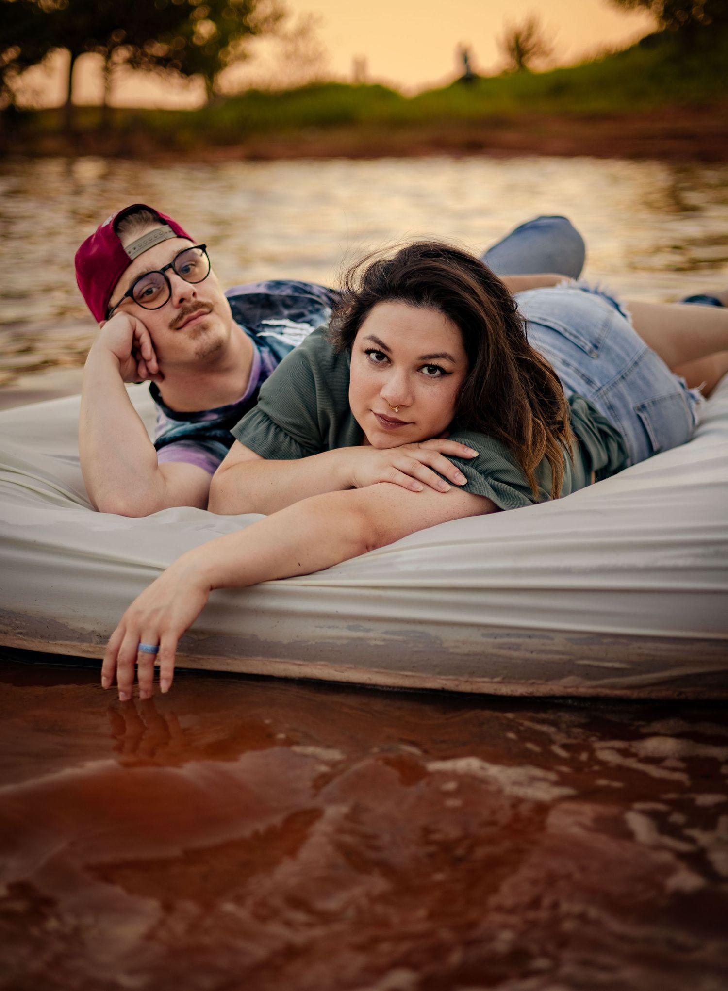Couple lying on a floating mattress on a lake, posing together during a warm sunset.
