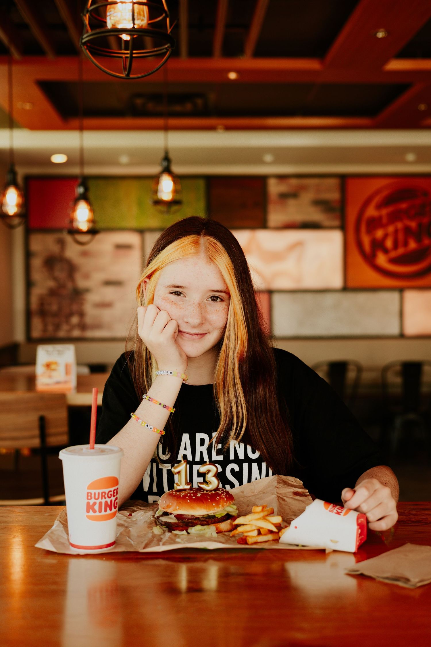 Teen girl smiling at table with Burger King burger, fries, and drink.