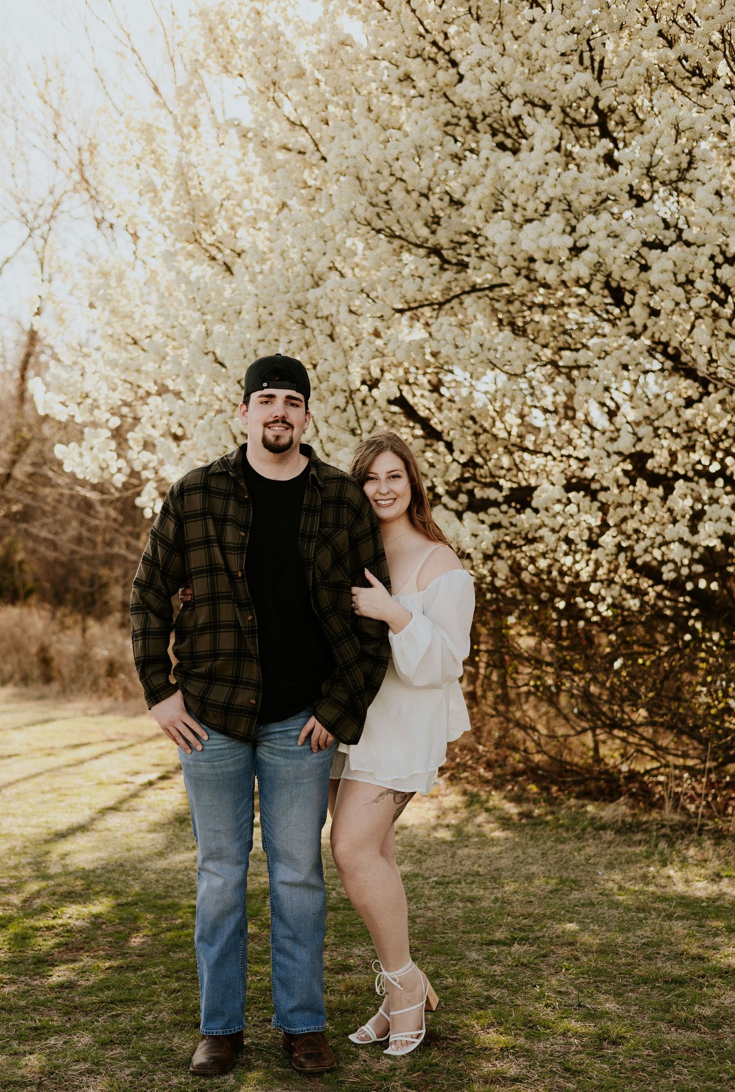 Smiling couple posing together in front of blooming white cherry blossom tree in spring.