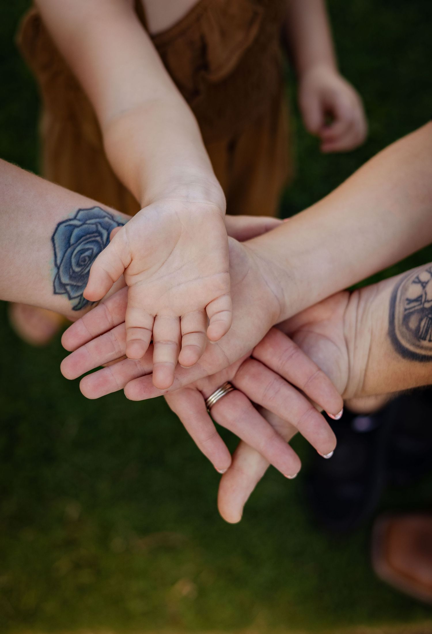 Close-up of family hands stacked together showing wrist tattoos of rose and anchor in outdoor setting.