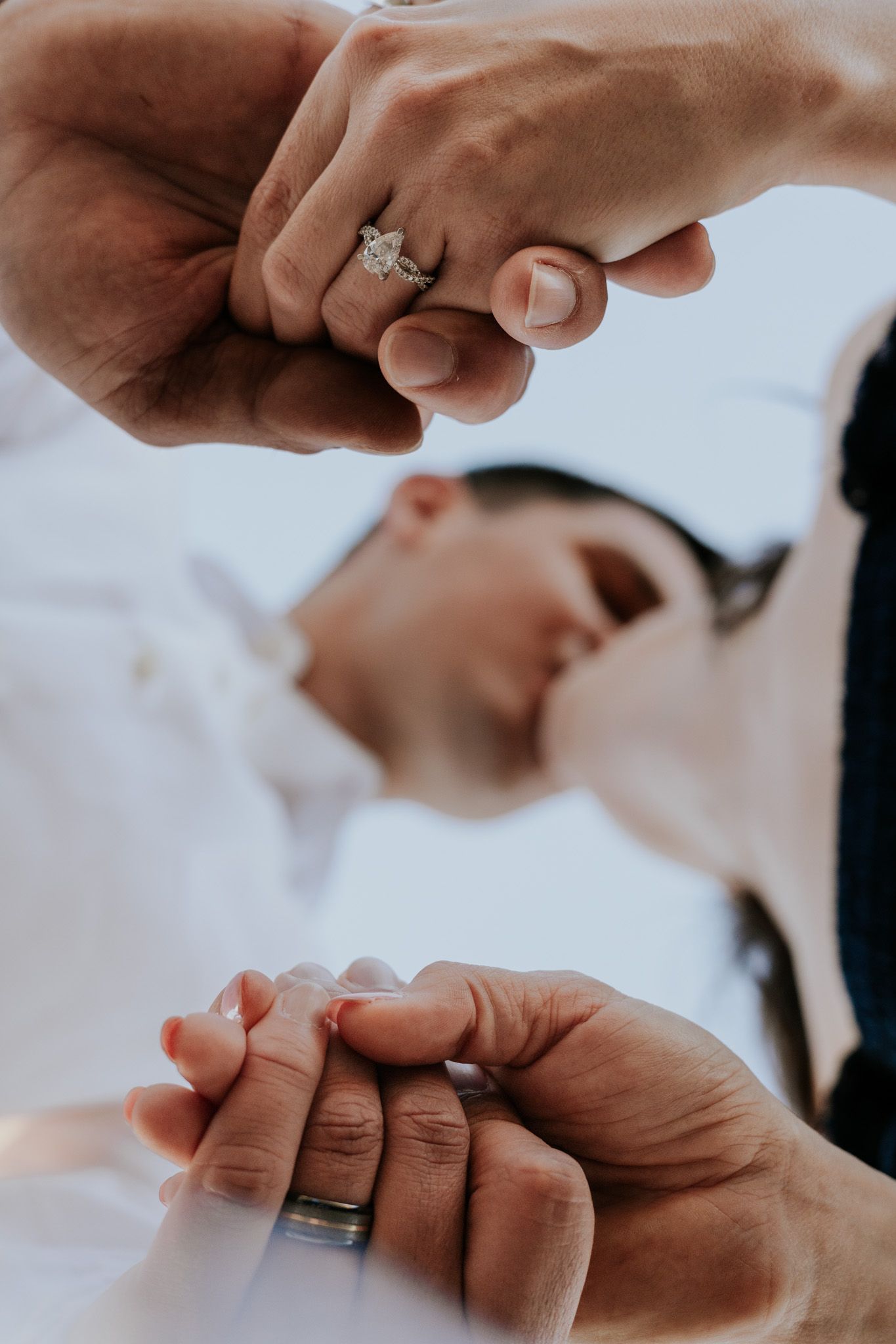 Close-up of couple holding hands showing diamond engagement ring and wedding band during romantic moment.
