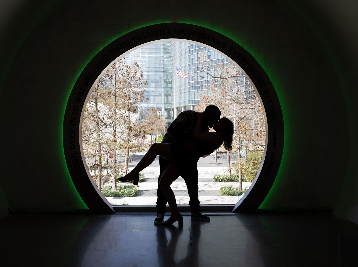 Silhouette of a couple sharing a romantic dip kiss framed by a large circular window with green lighting.