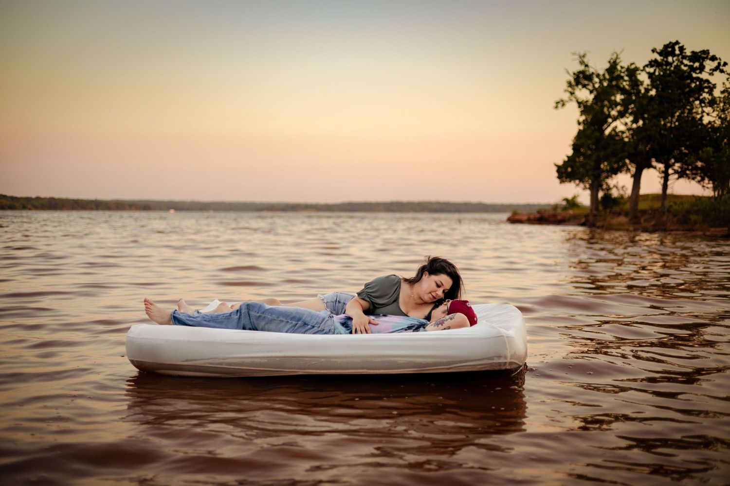 Couple relaxing on a white inflatable raft floating on a calm lake at golden sunset hour.