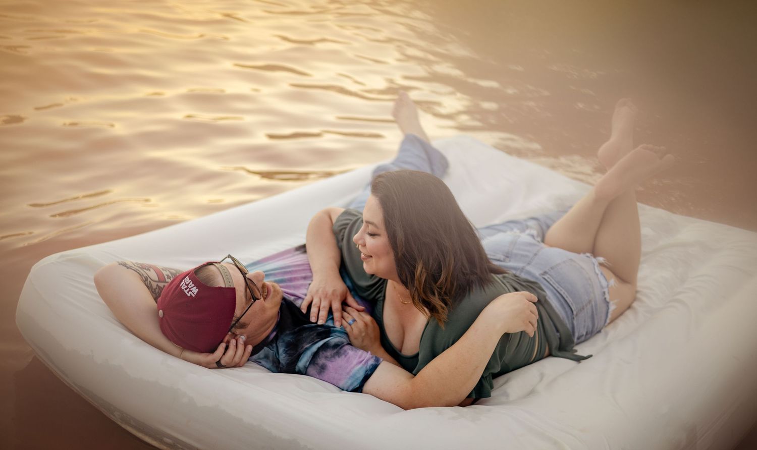 Two people relaxing and laughing together on a floating raft on a golden sunset lake.