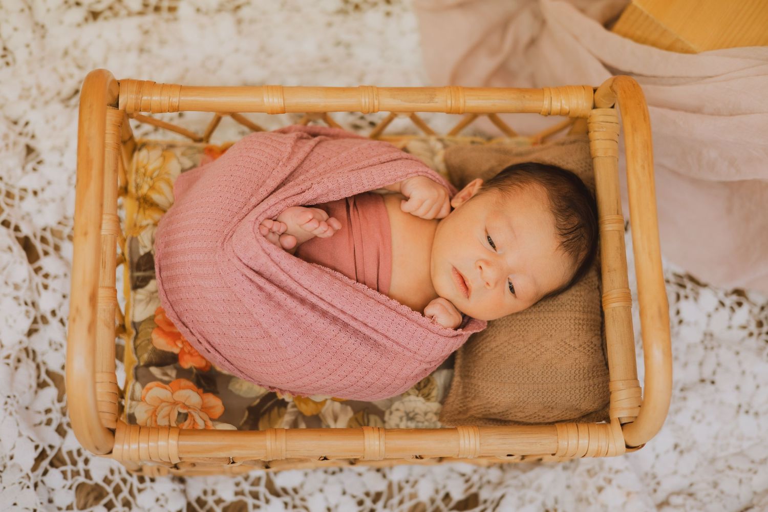 Sleeping newborn baby wrapped in pink swaddle resting in small rattan wooden basket.