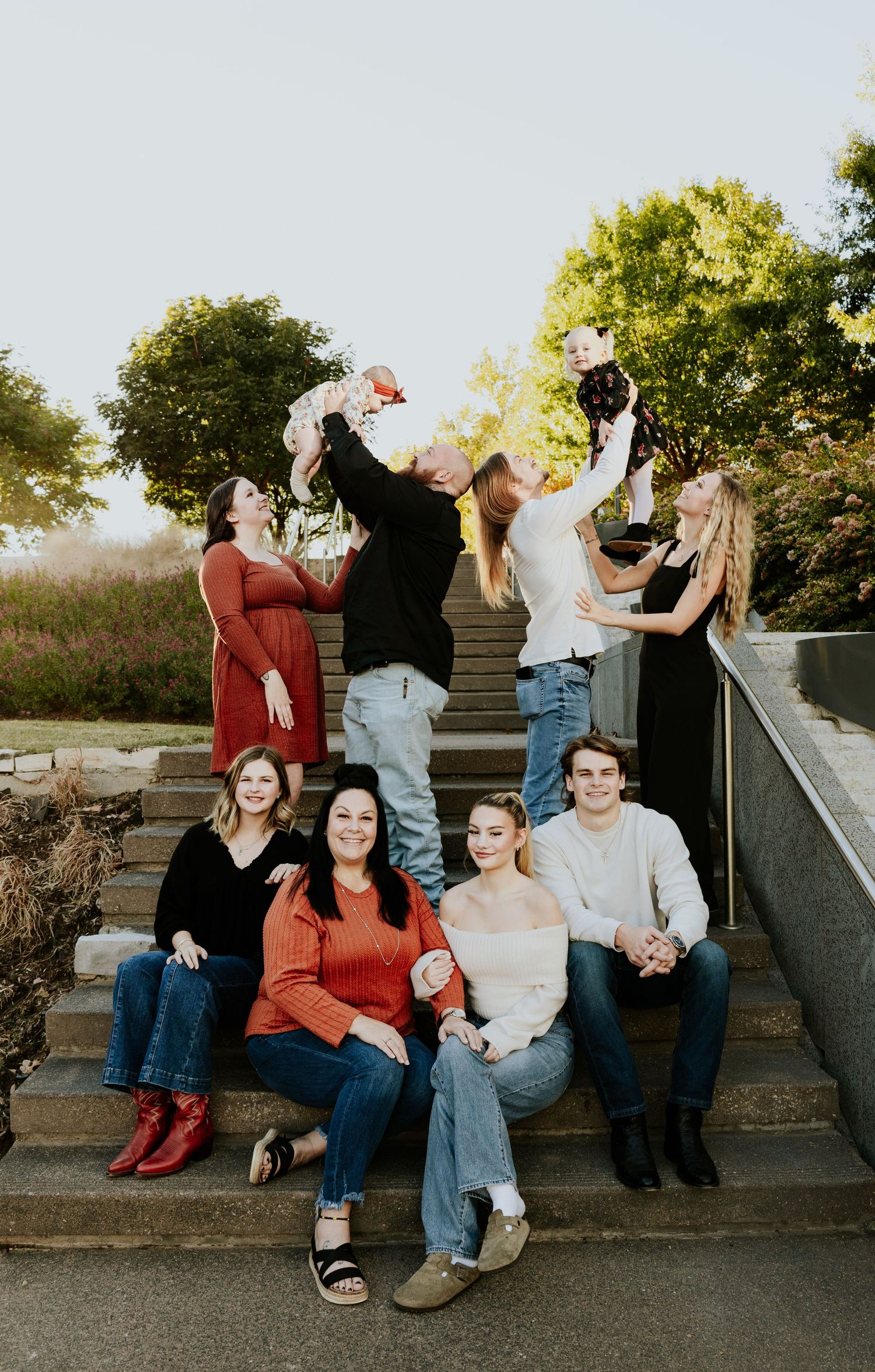 Large family group posing on outdoor stone steps at golden hour with babies.