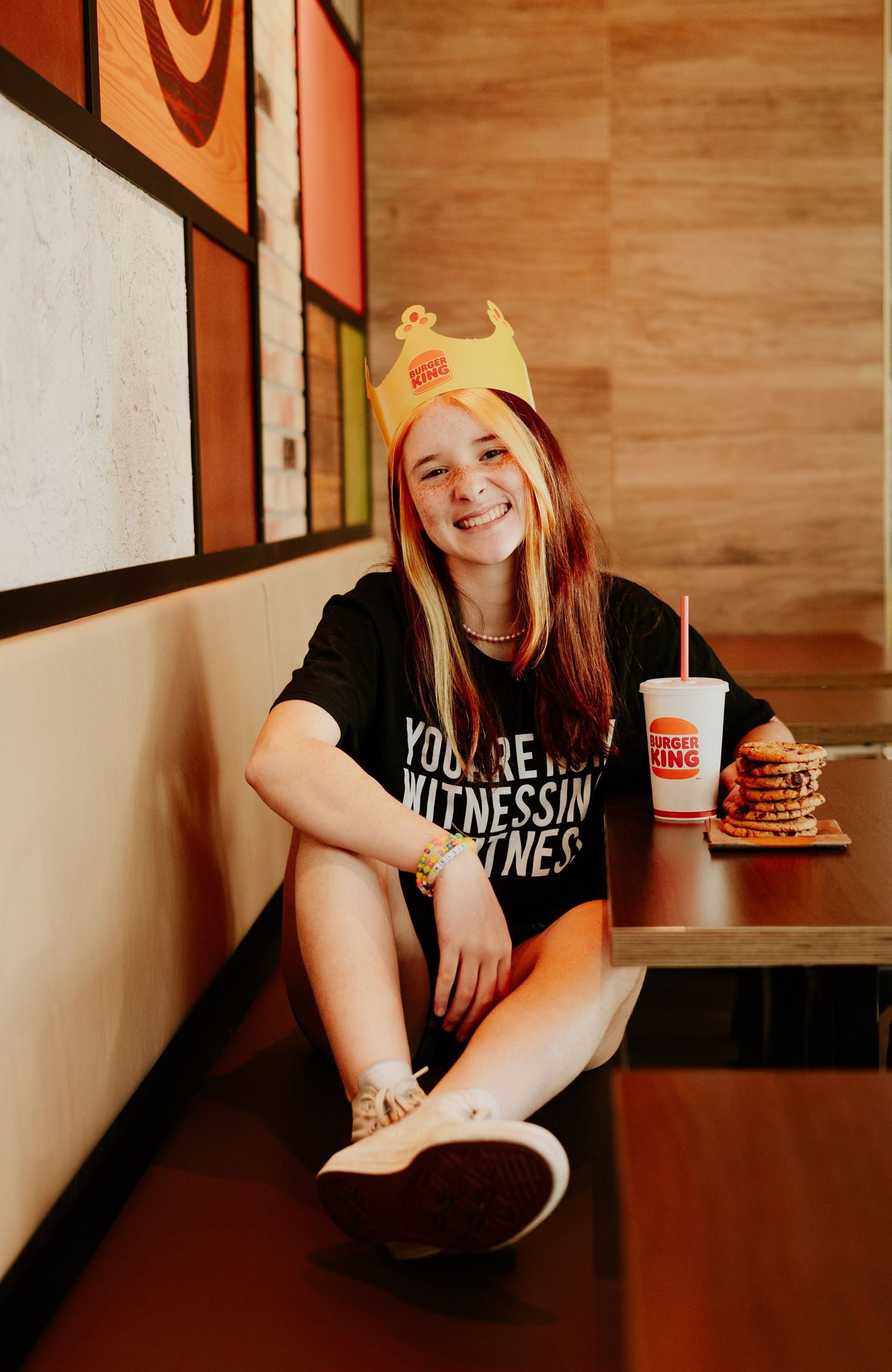 Smiling teen girl wearing Burger King crown hat sitting in restaurant booth.