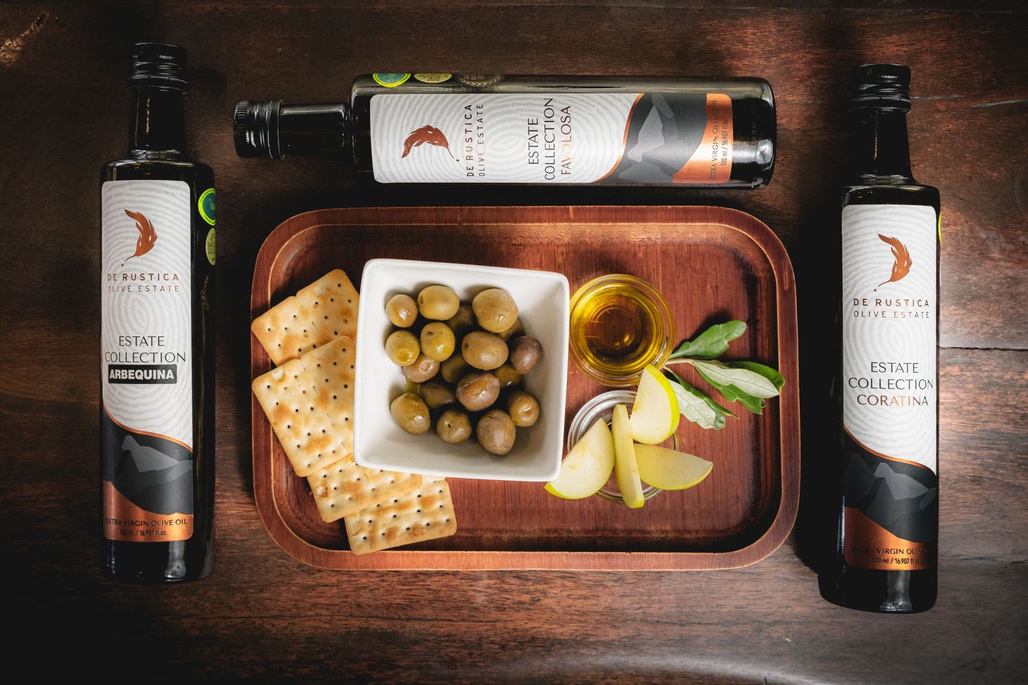 Overhead view of wine bottles, crackers, and olives arranged on a wooden serving board.