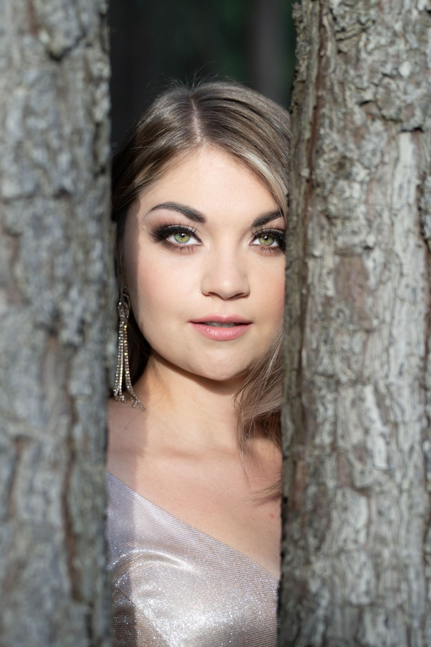 Woman peeking through trees wearing natural makeup outdoors
