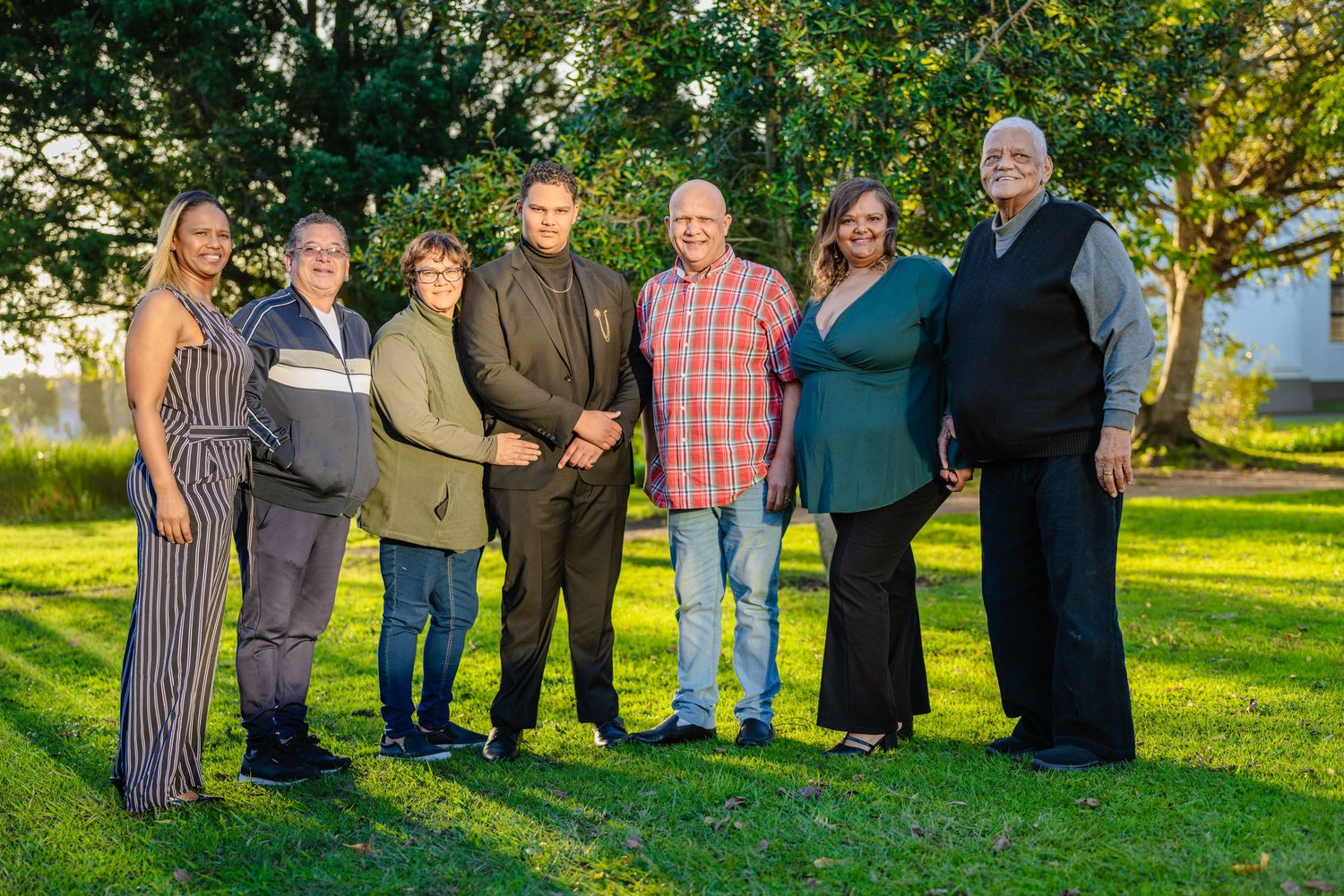 Large family group portrait taken outdoors in a lush green park setting.