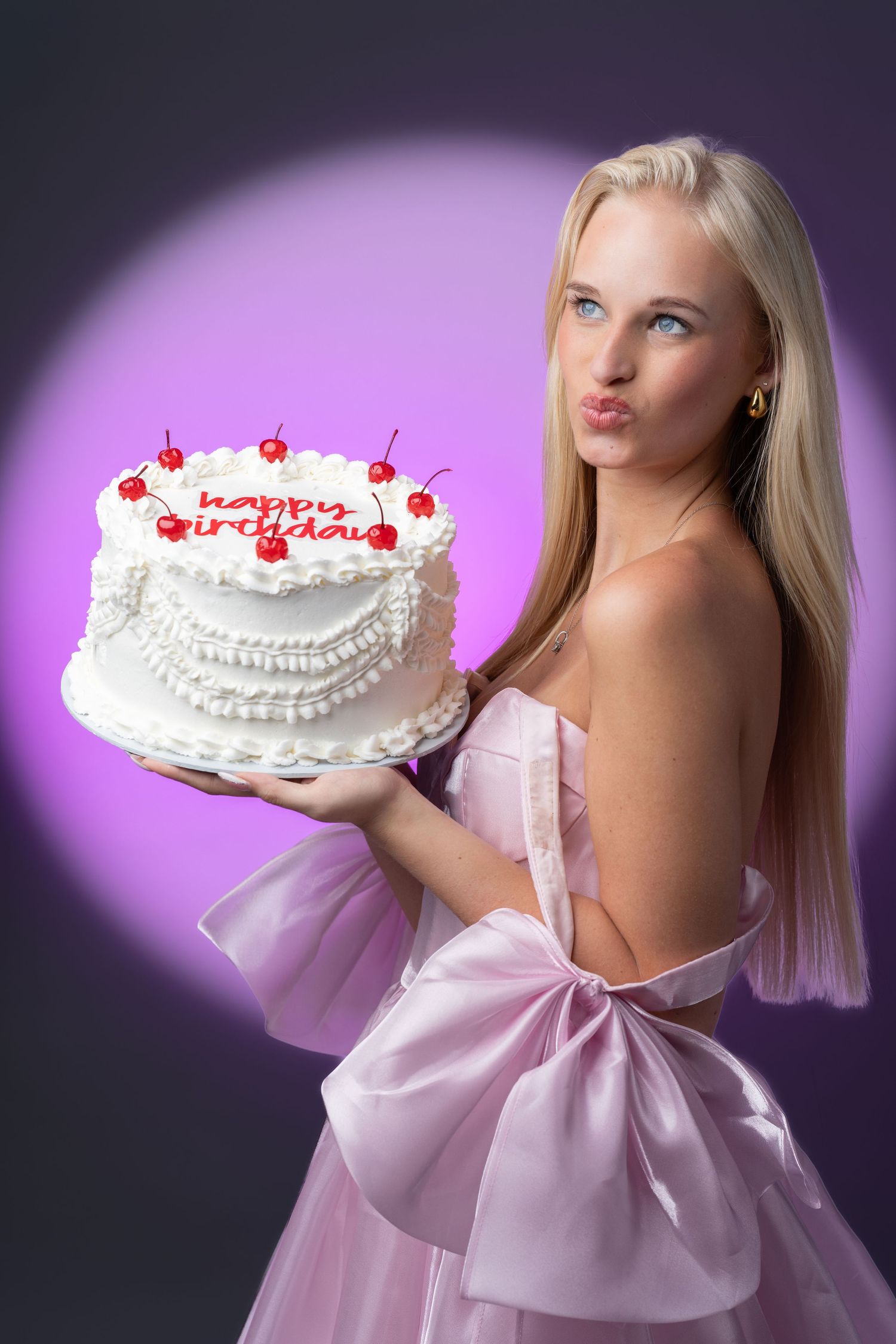 A white birthday cake with red cherries and text held against a purple background.