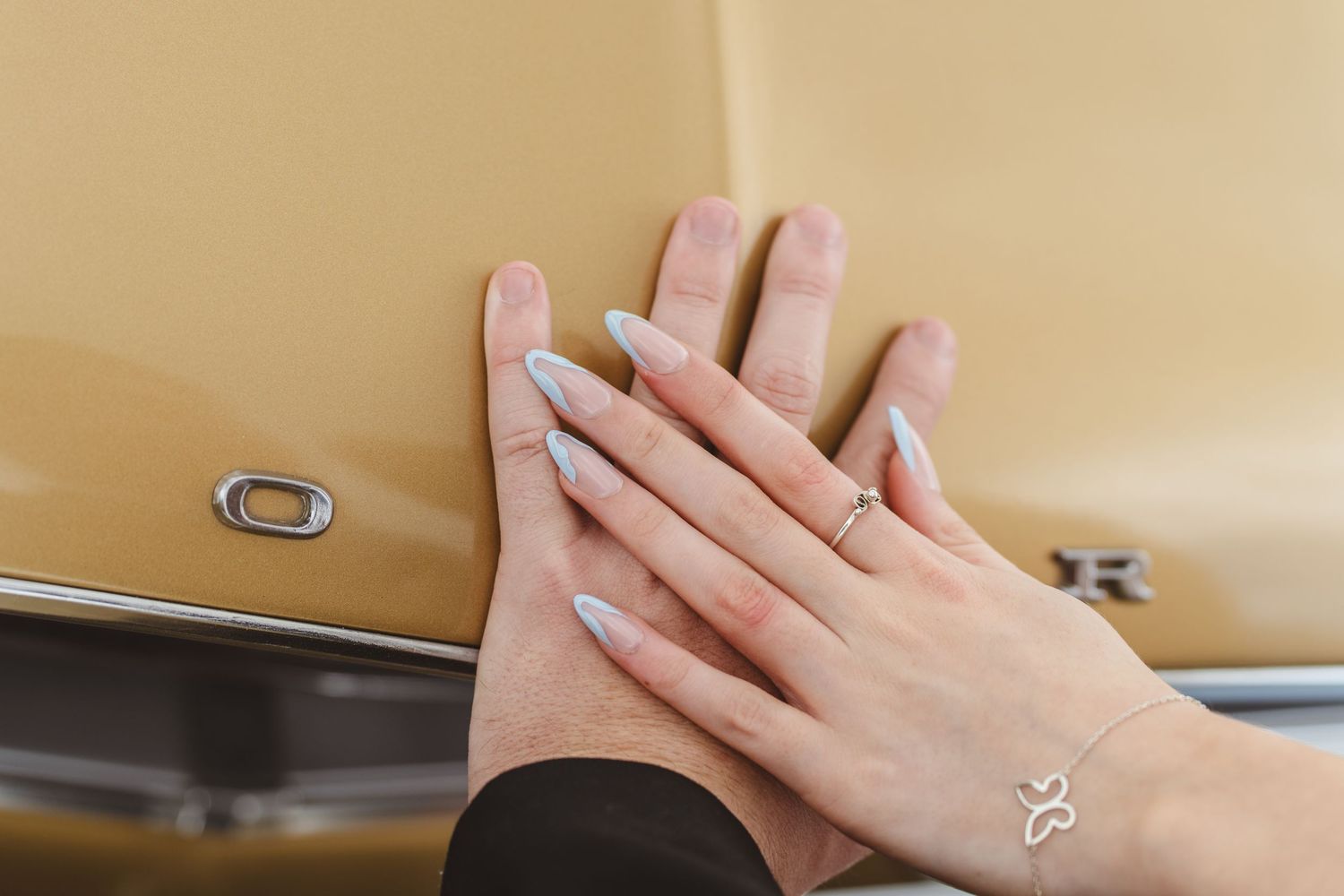 Close-up of hands with an engagement ring resting on a beige surface.