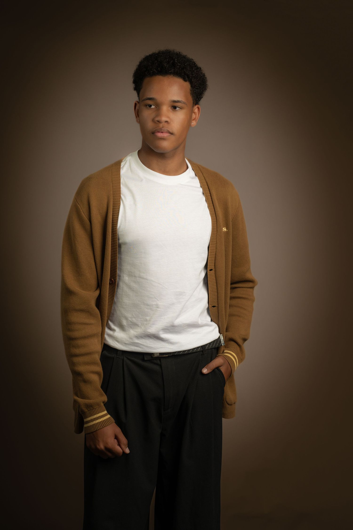 A portrait of someone wearing a brown cardigan over a white t-shirt against a dark background.