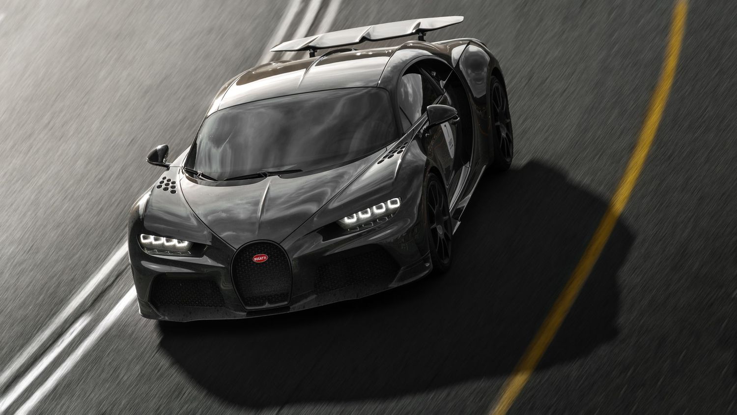 Sleek black Bugatti Chiron supercar captured from above on a winding road, showcasing its aerodynamic carbon fiber body.