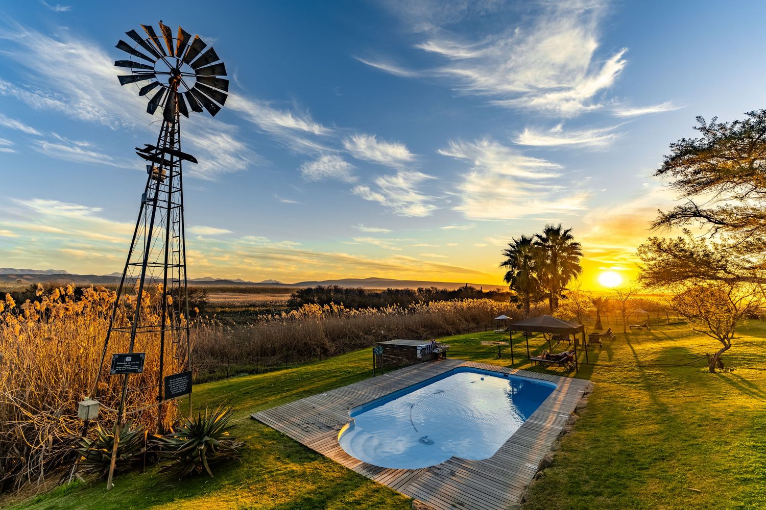 Karoo sunset with a windmill and swimming pool in the foreground with a vast karoo valley view in the background