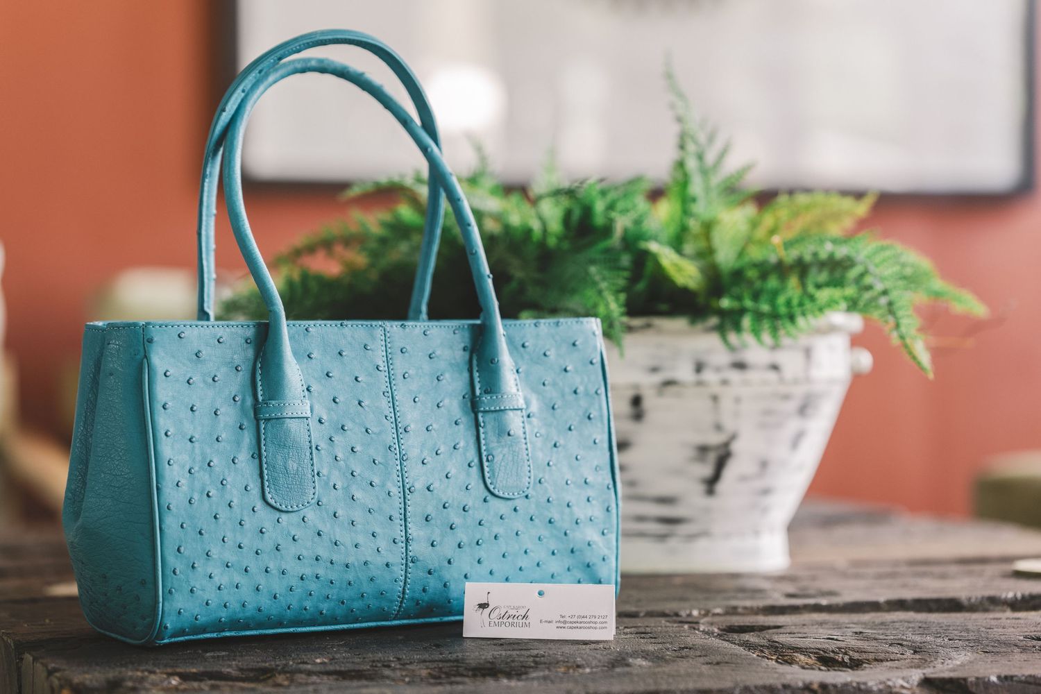 Collection of teal blue ostrich leather handbags displayed on wooden surface.