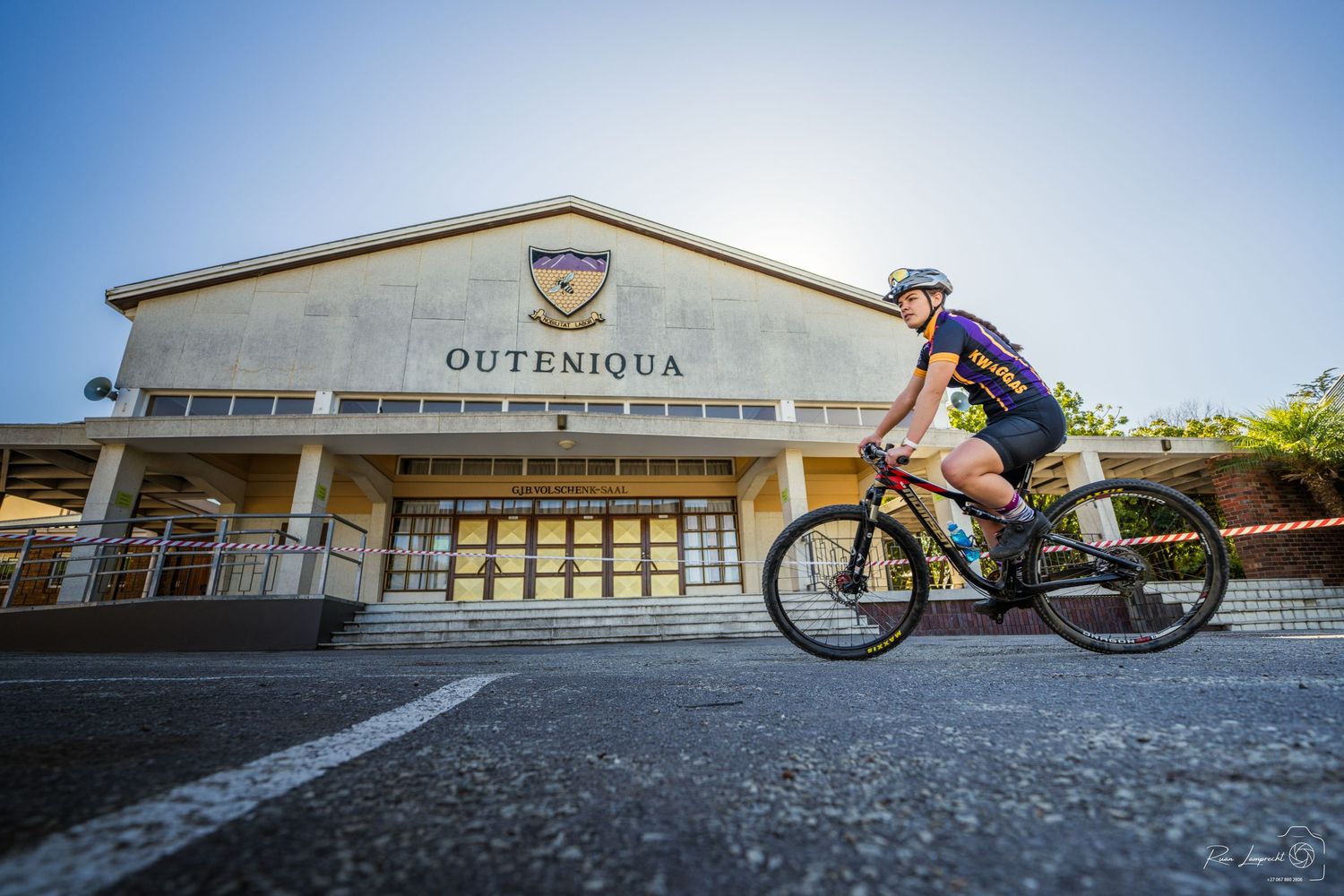 Photo of a cyclist wearing her school colours riding past the main hall of the school
